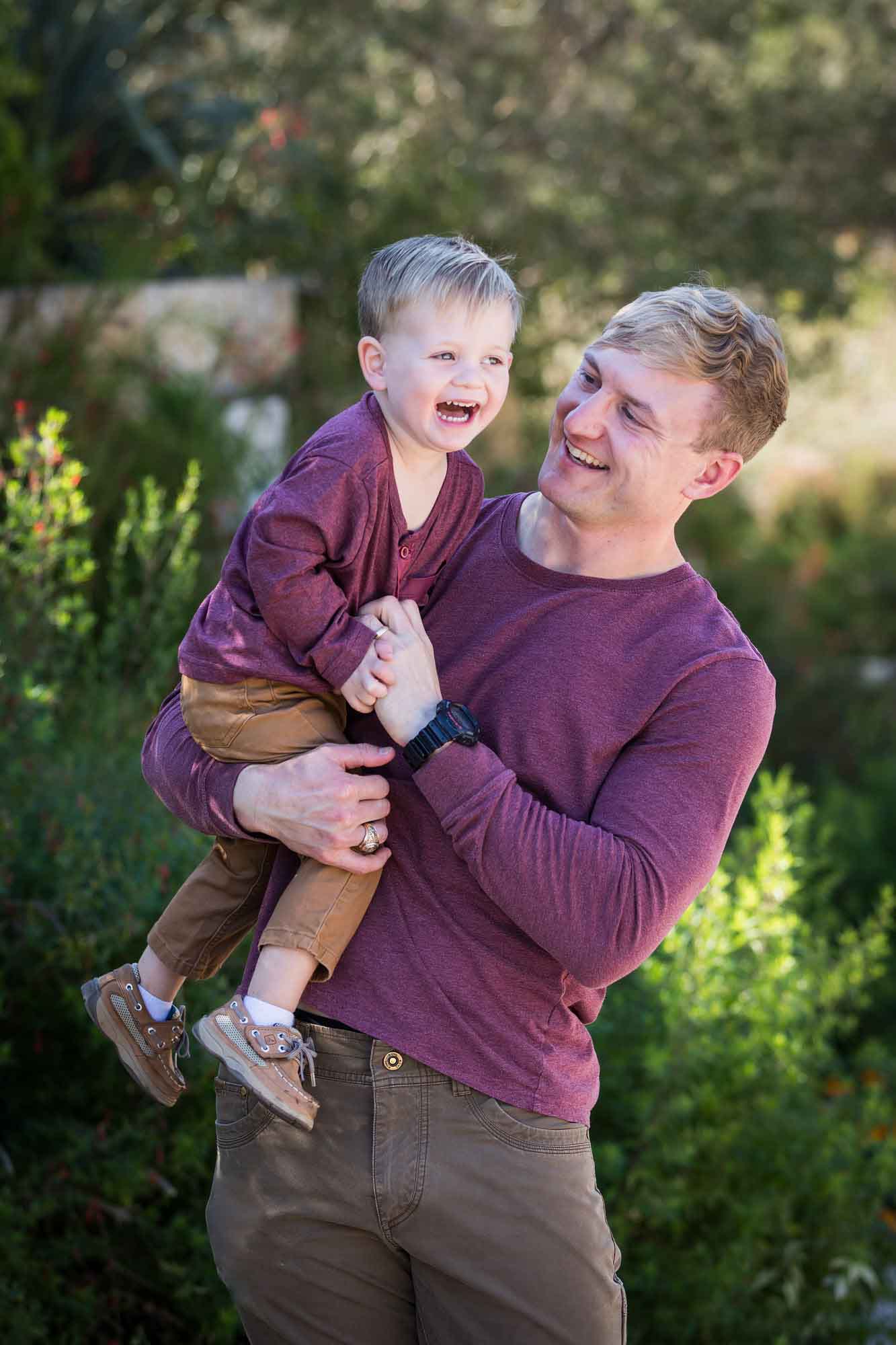 San Antonio Botanical Gardens family portrait of man wearing purple shirt and brown pants playing with little boy wearing purple shirt and tan pants