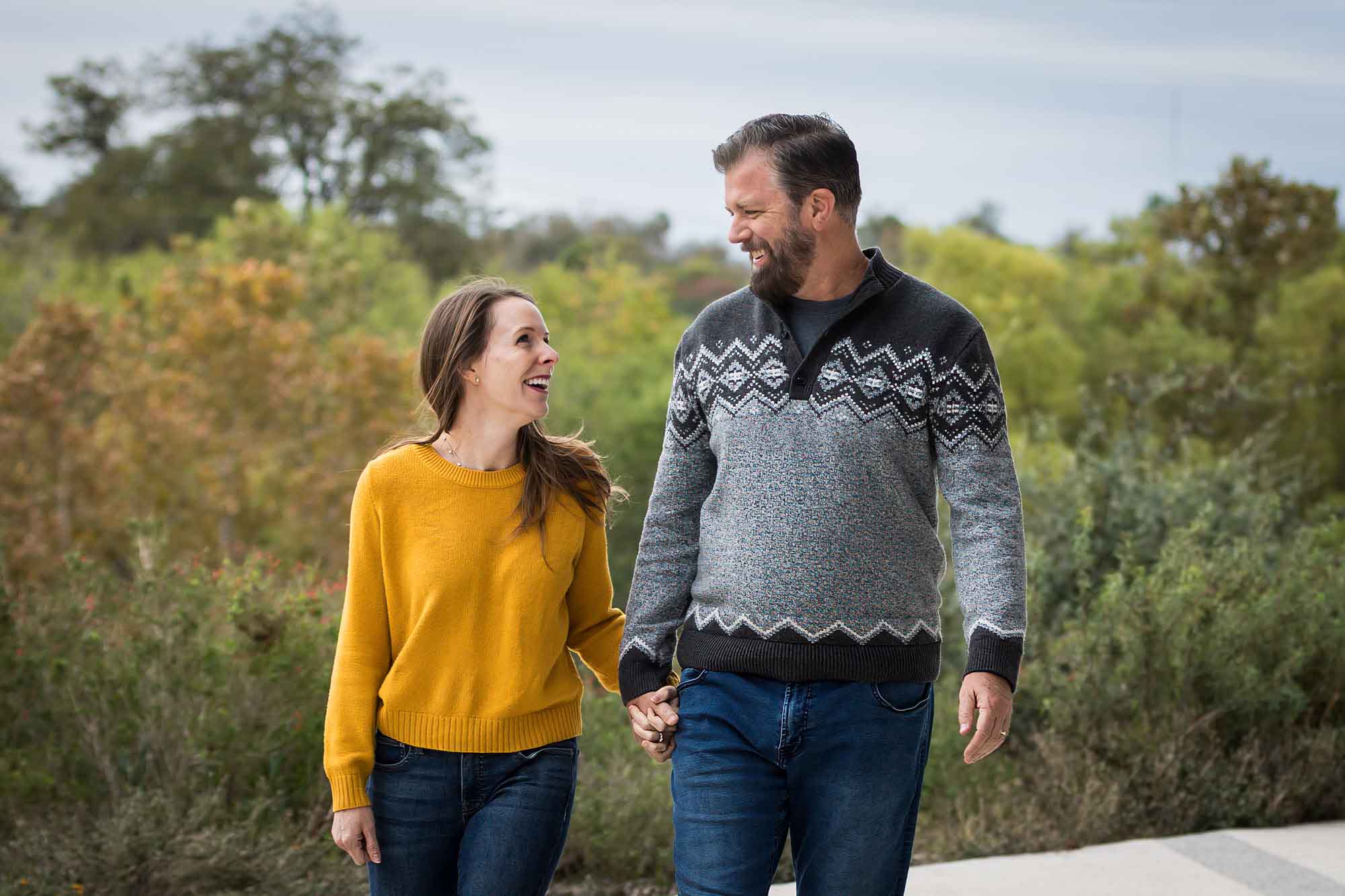 Man wearing grey sweater holding hands with woman wearing yellow sweater and jeans during a Confluence Park family portrait session