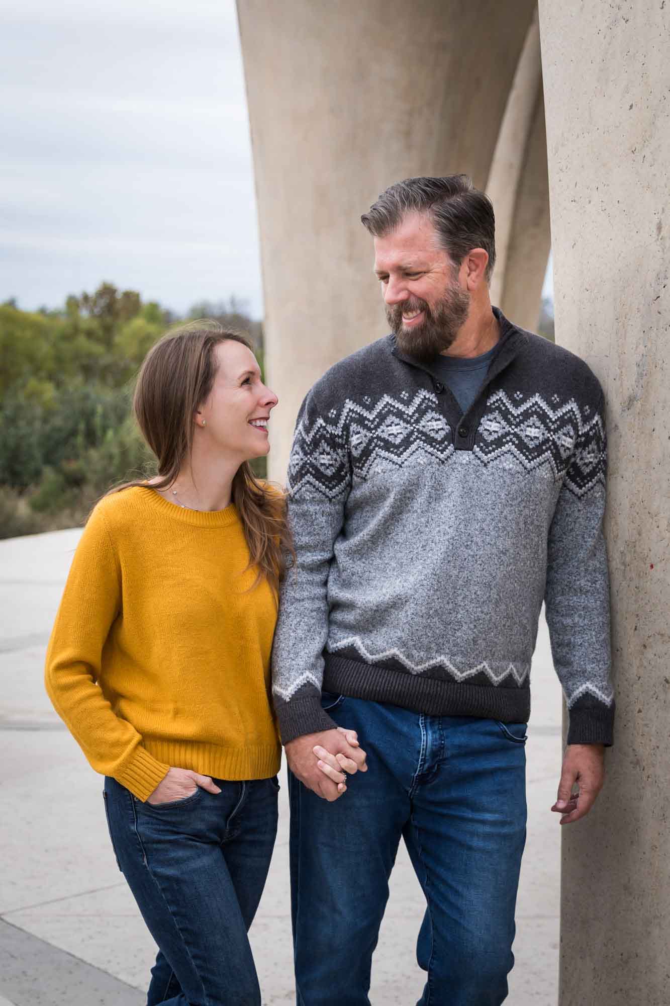Man wearing grey sweater holding hands with woman wearing yellow sweater and jeans during a Confluence Park family portrait session