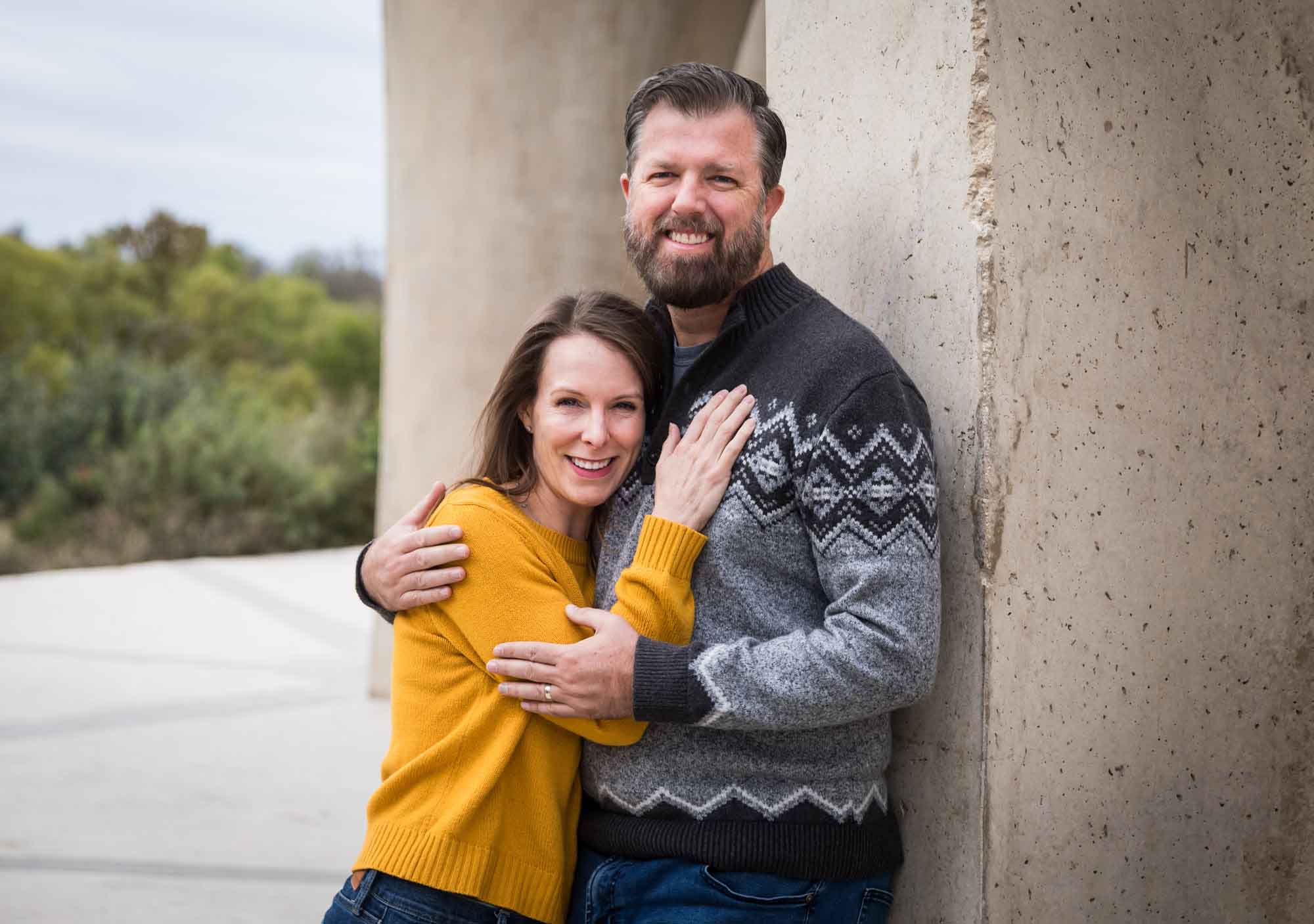 Man wearing grey sweater hugging woman wearing yellow sweater and jeans during a Confluence Park family portrait session