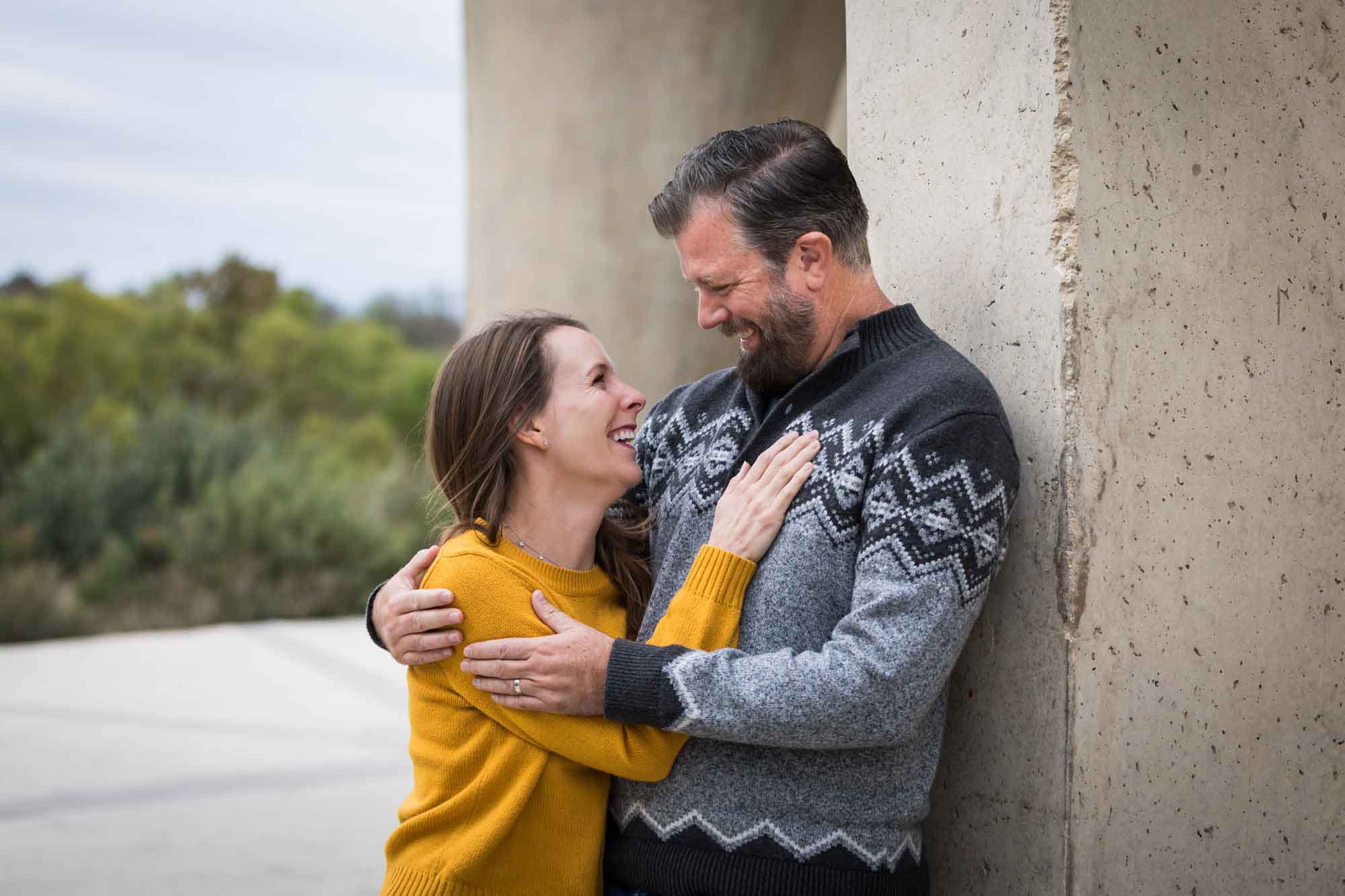 Man wearing grey sweater hugging woman wearing yellow sweater and jeans during a Confluence Park family portrait session