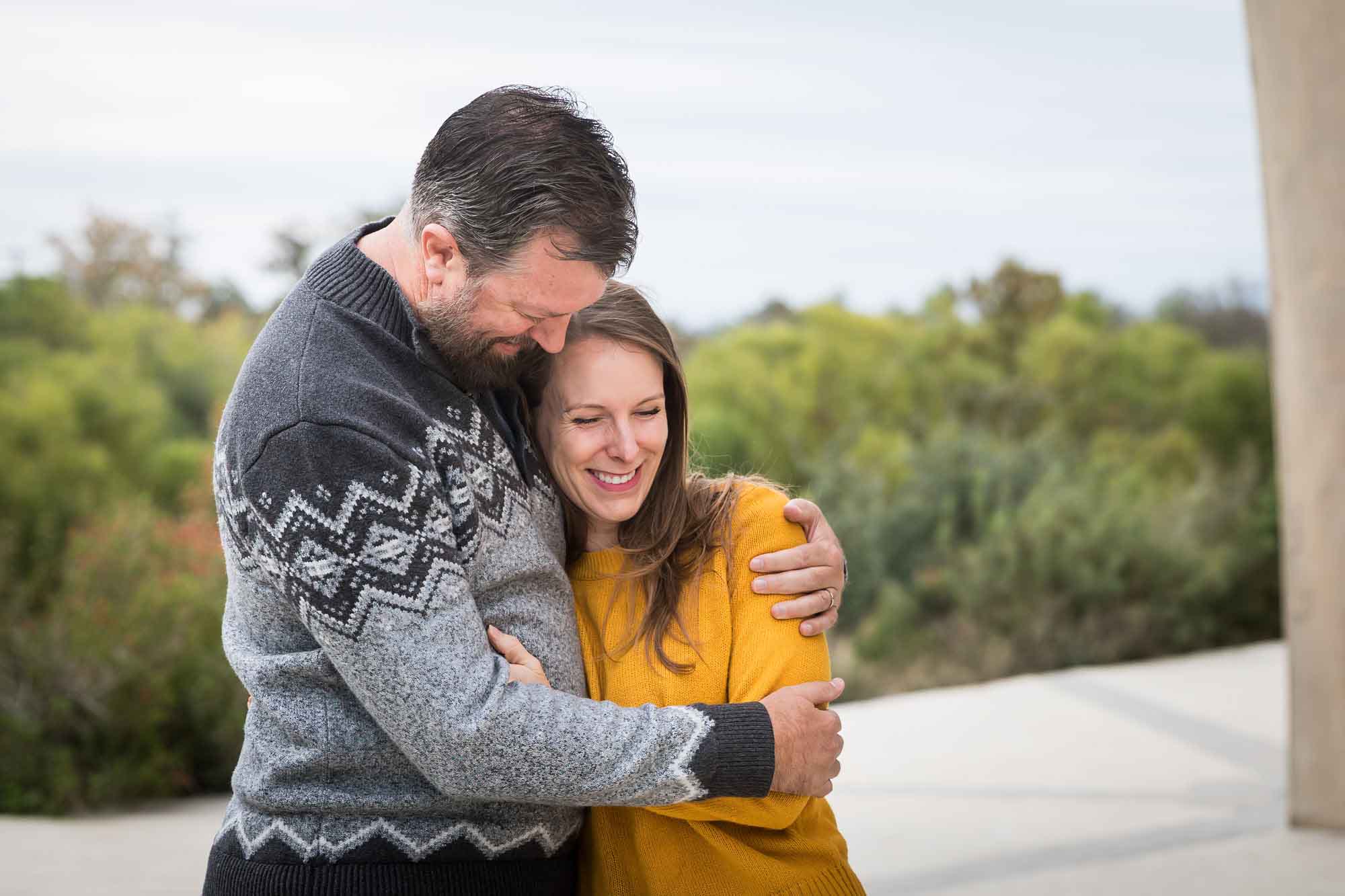 Man wearing grey sweater hugging woman wearing yellow sweater and jeans during a Confluence Park family portrait session