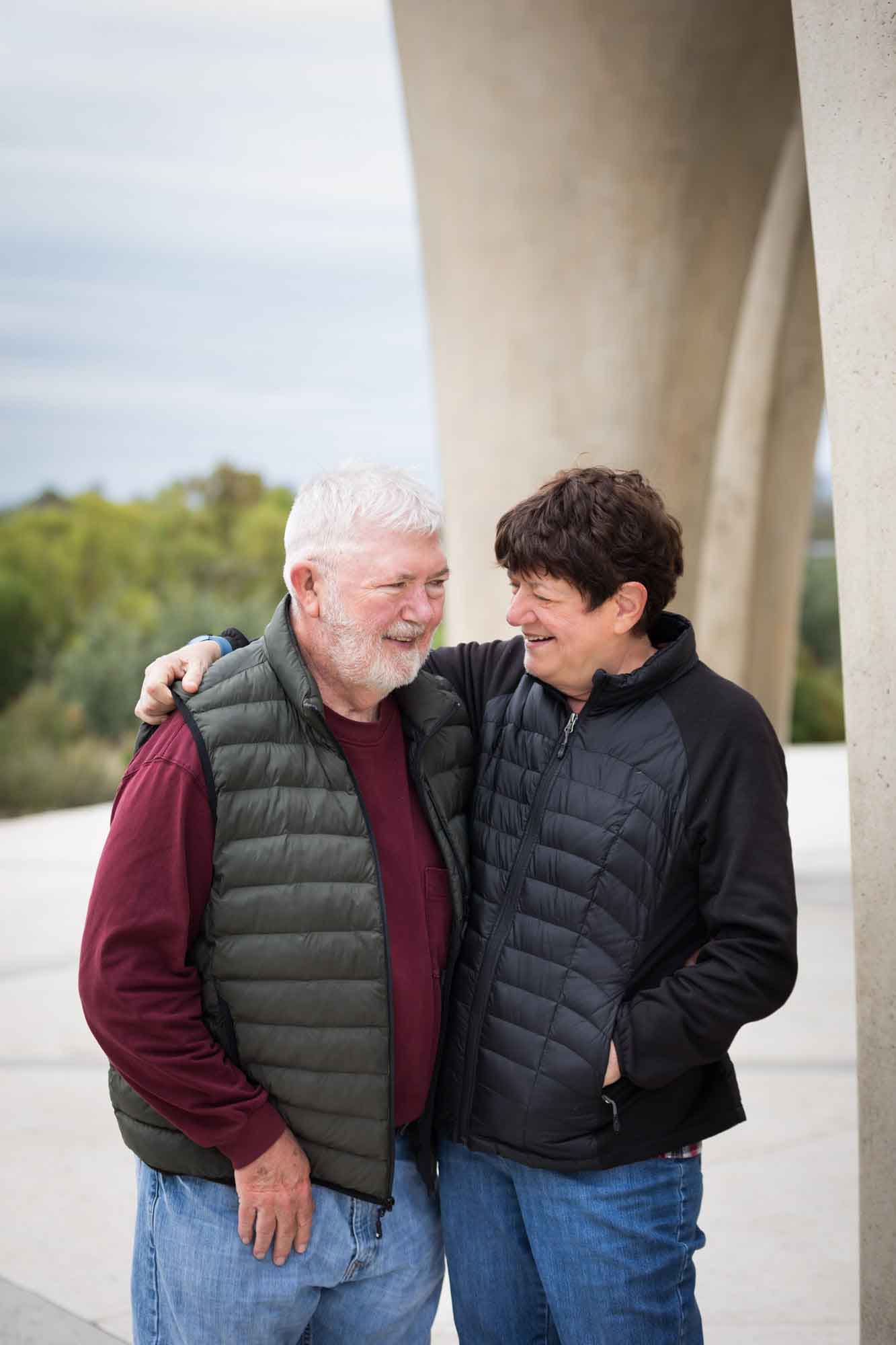 Older man wearing puffy vest and maroon shirt hugging an older woman wearing black sweater during a Confluence Park family portrait session