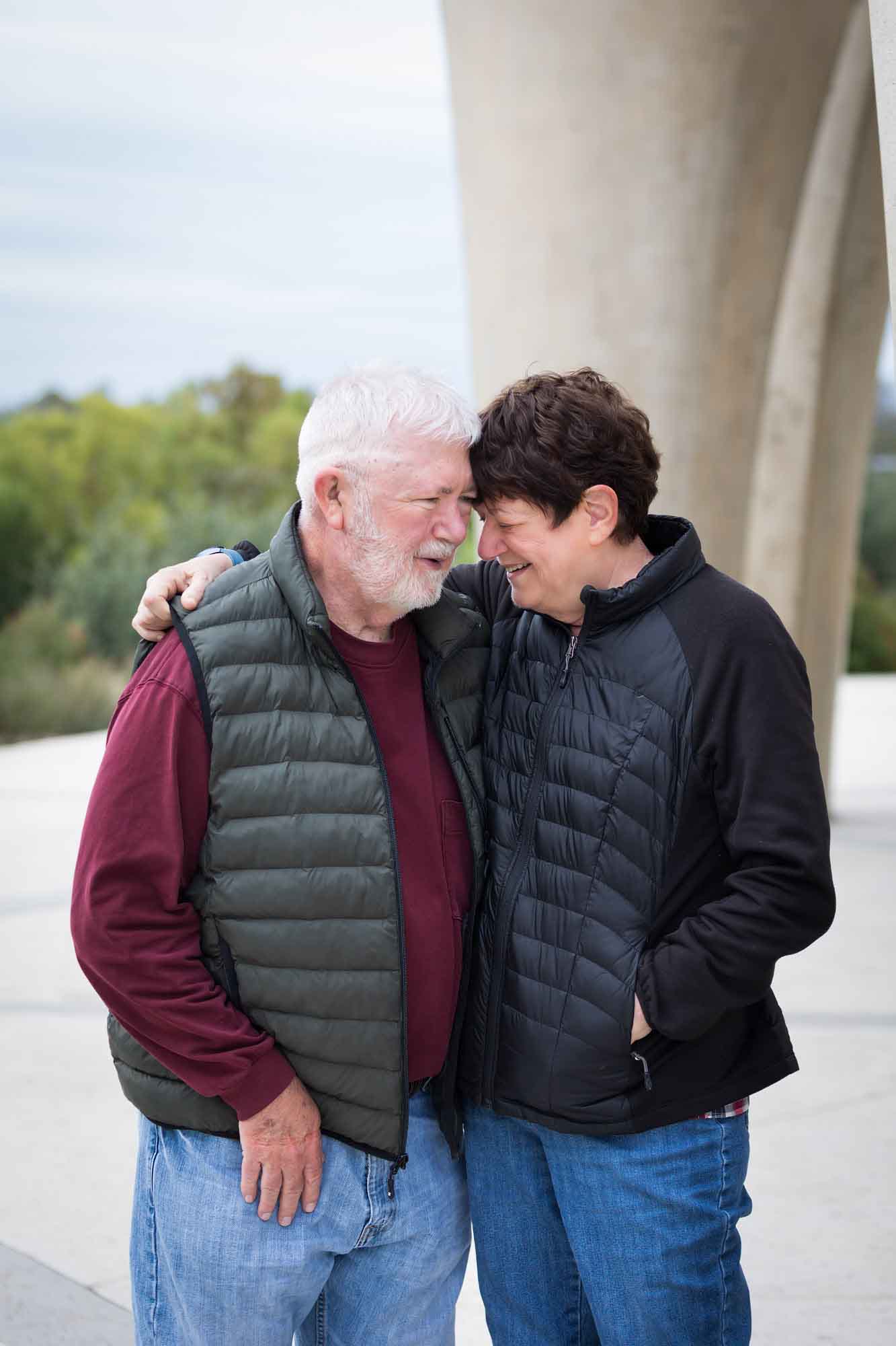 Older man wearing puffy vest and maroon shirt hugging an older woman wearing black sweater during a Confluence Park family portrait session