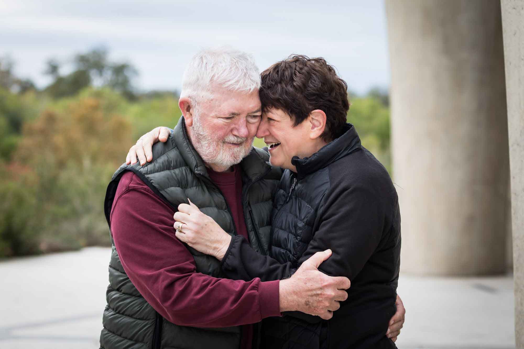 Older man wearing puffy vest and maroon shirt hugging an older woman wearing black sweater during a Confluence Park family portrait session