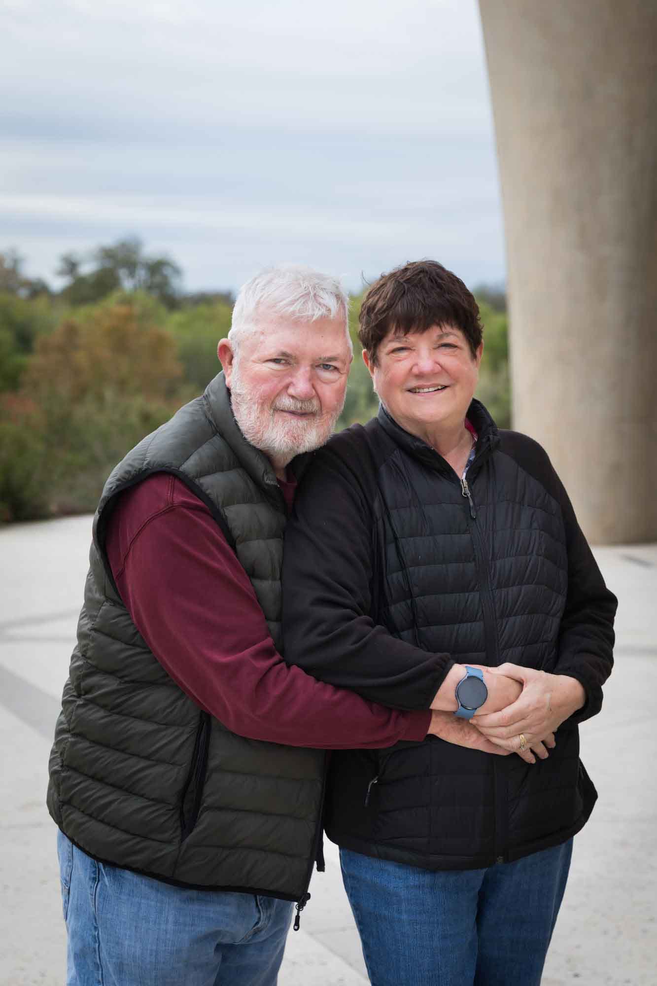 Older man wearing puffy vest and maroon shirt hugging an older woman wearing black sweater during a Confluence Park family portrait session