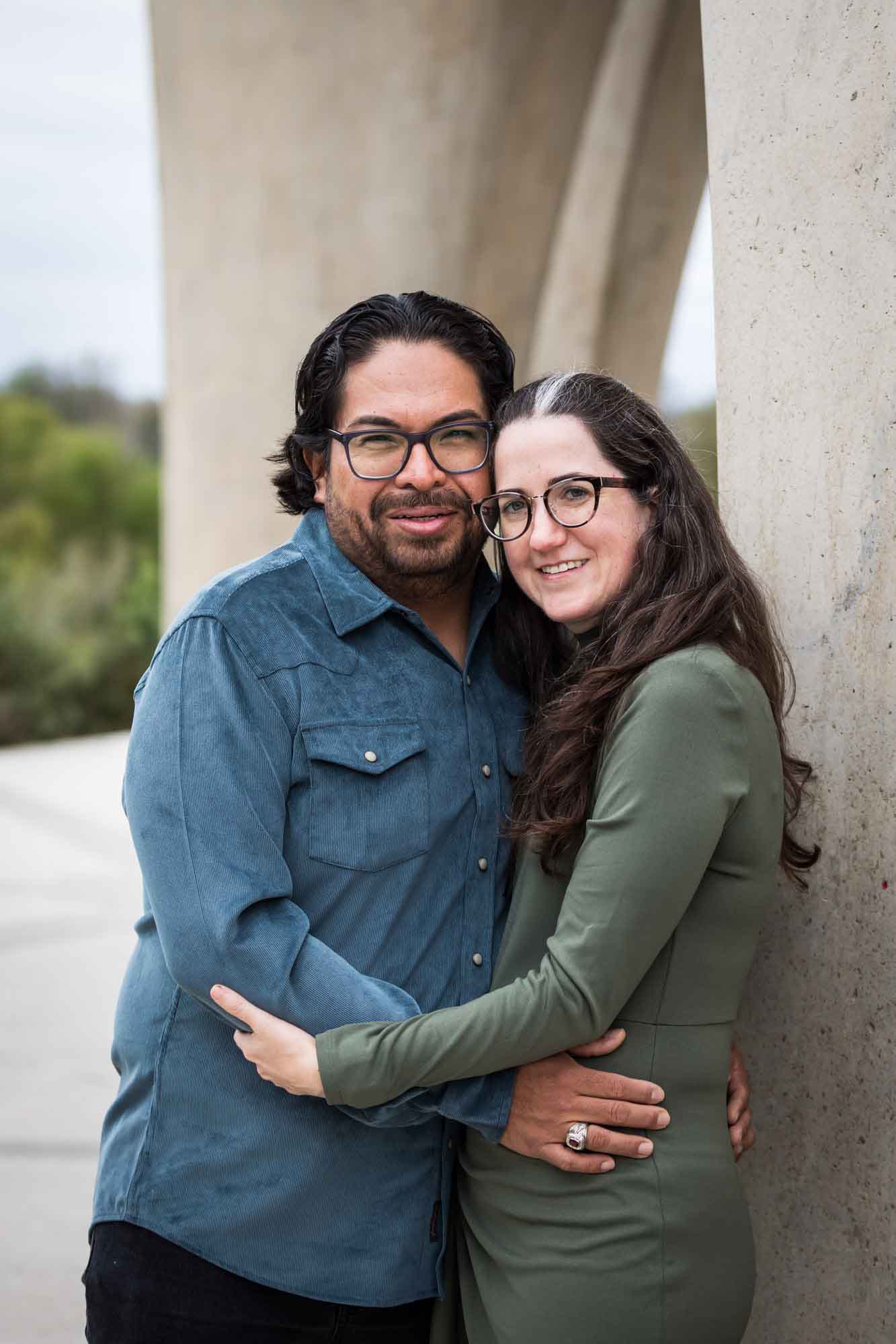 Man wearing denim long-sleeved shirt being hugging a woman wearing green long-sleeved shirt during a Confluence Park family portrait session