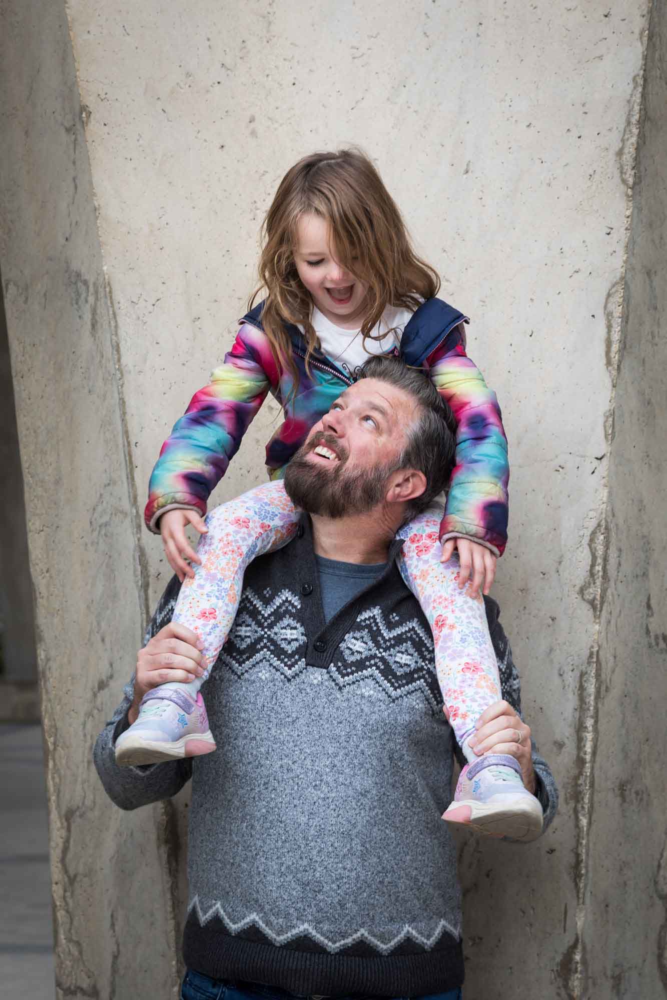 Father wearing grey sweater holding little girl wearing multicolored sweater on his shoulders during a Confluence Park family portrait session