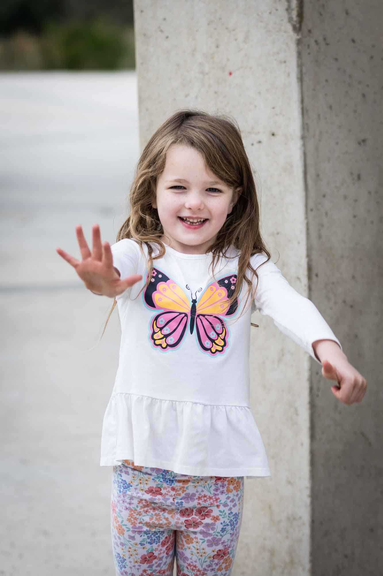 Little girl wearing butterfly-printed dress with hands outstretched during a Confluence Park family portrait session