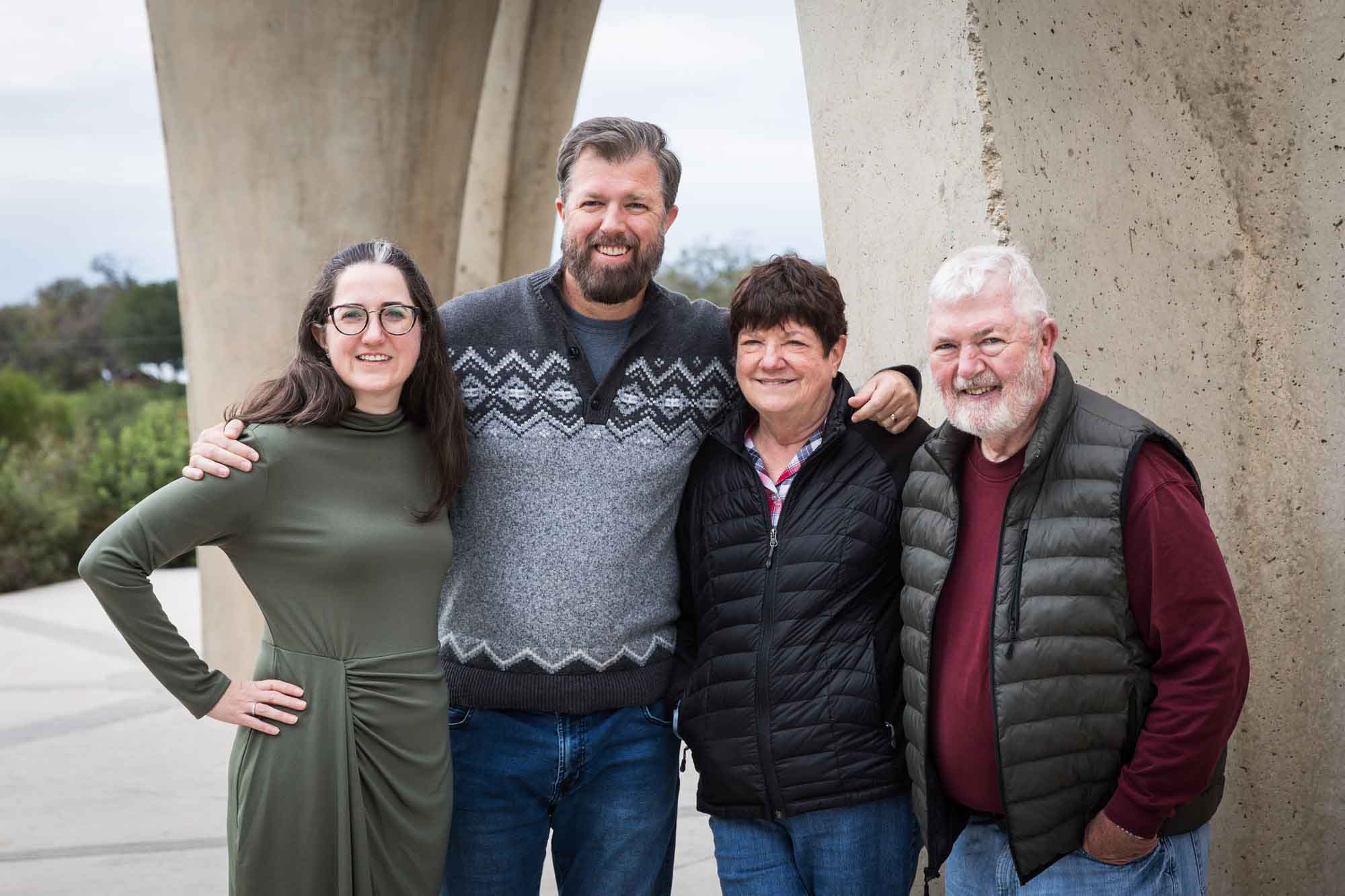Older man and woman with arms around man wearing grey sweater and woman wearing green dress in front of concrete arch during a Confluence Park family portrait session