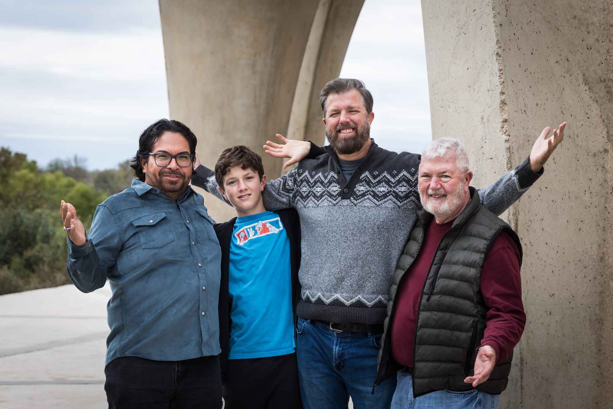 Four men of varying ages with arms around one another standing in front of concrete arch during a Confluence Park family portrait session