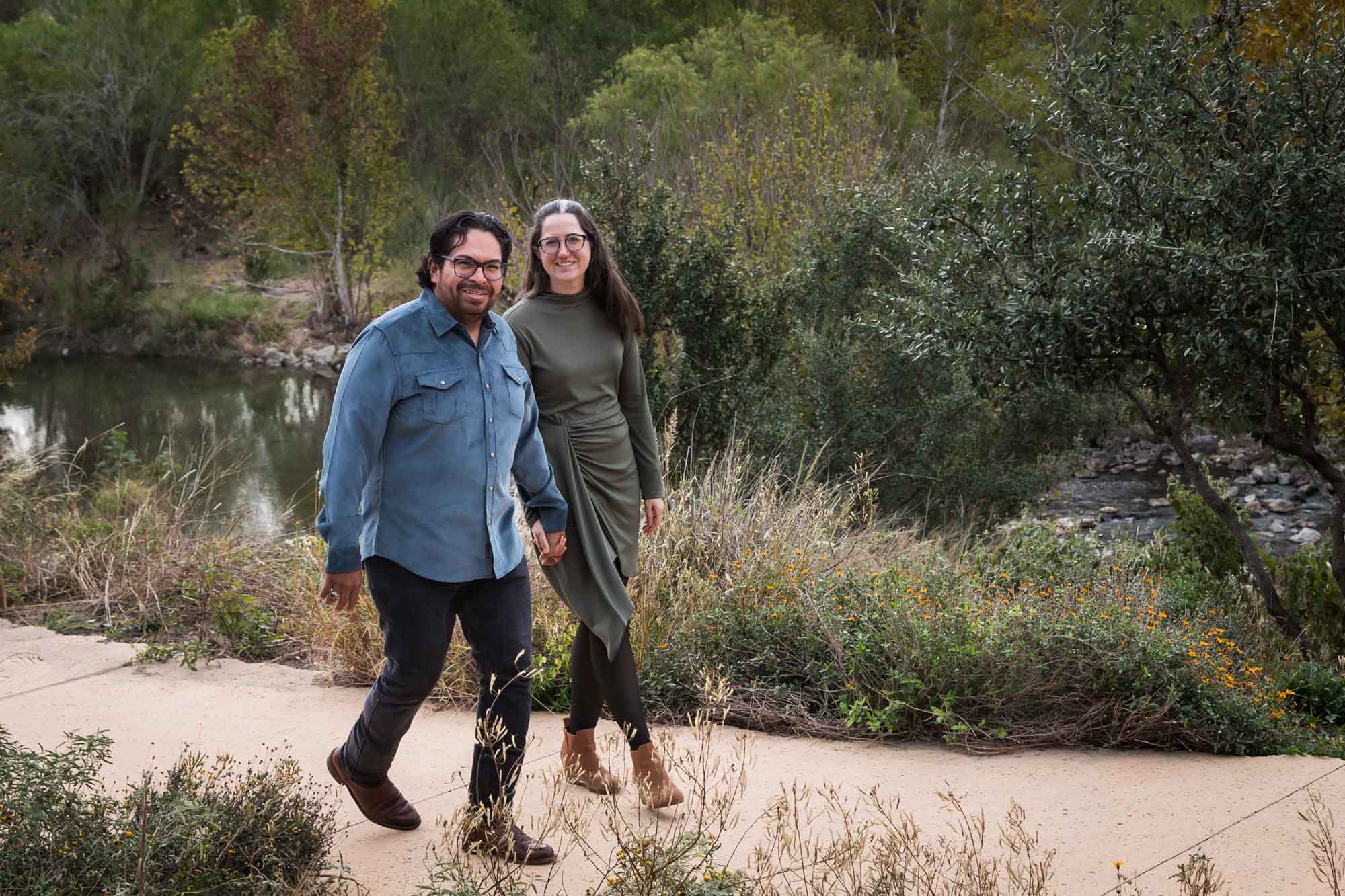 Man wearing denim long-sleeved shirt walking with woman wearing green dress during a Confluence Park family portrait session