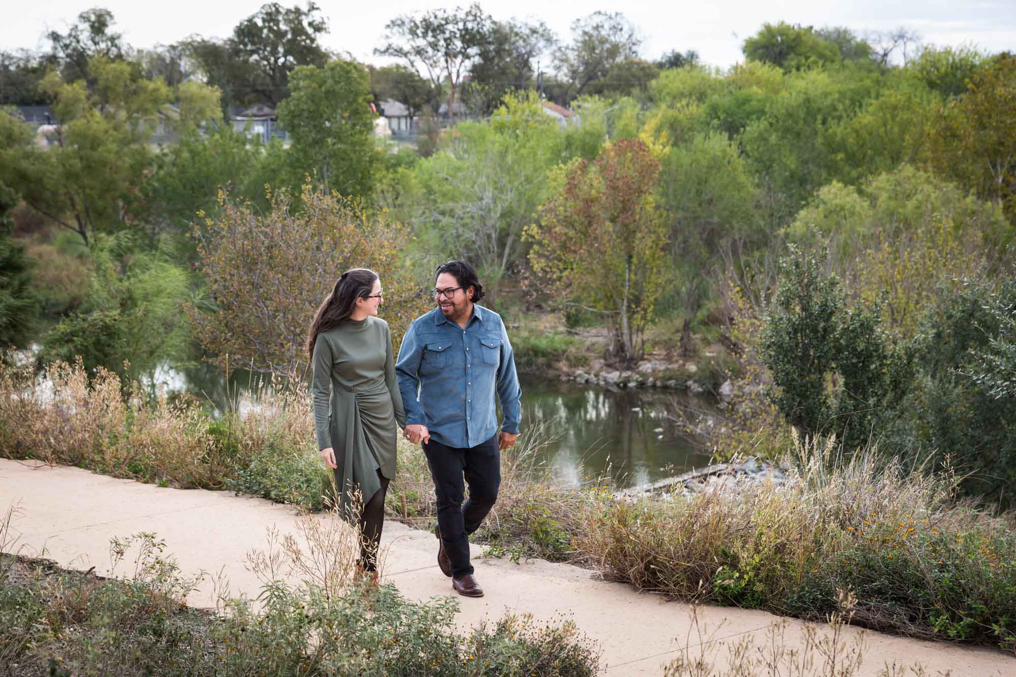 Man wearing denim long-sleeved shirt walking with woman wearing green dress during a Confluence Park family portrait session
