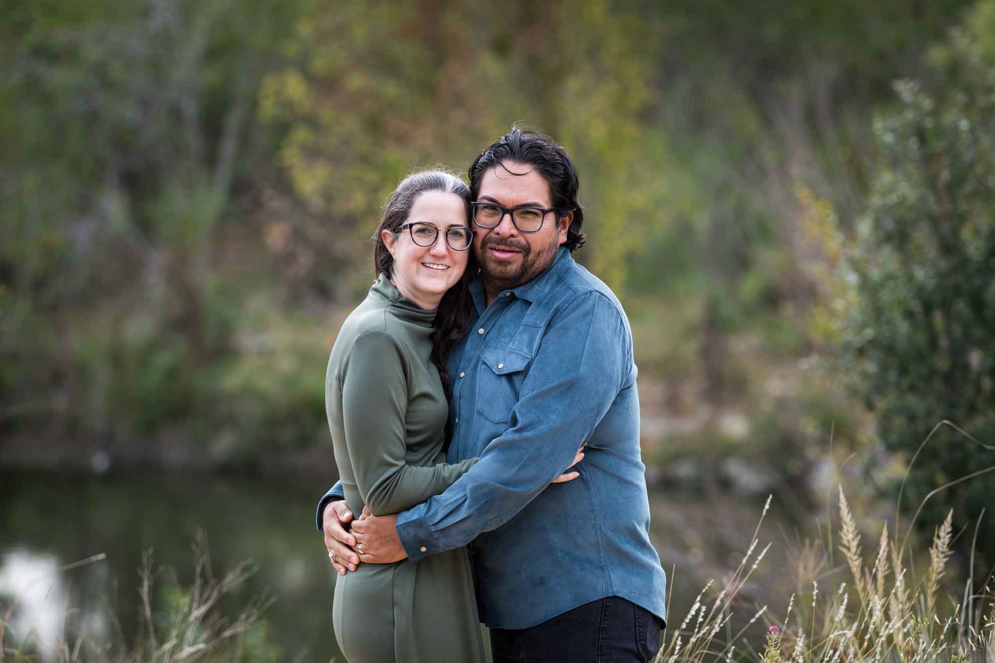 Man wearing denim long-sleeved shirt hugging woman wearing green dress during a Confluence Park family portrait session