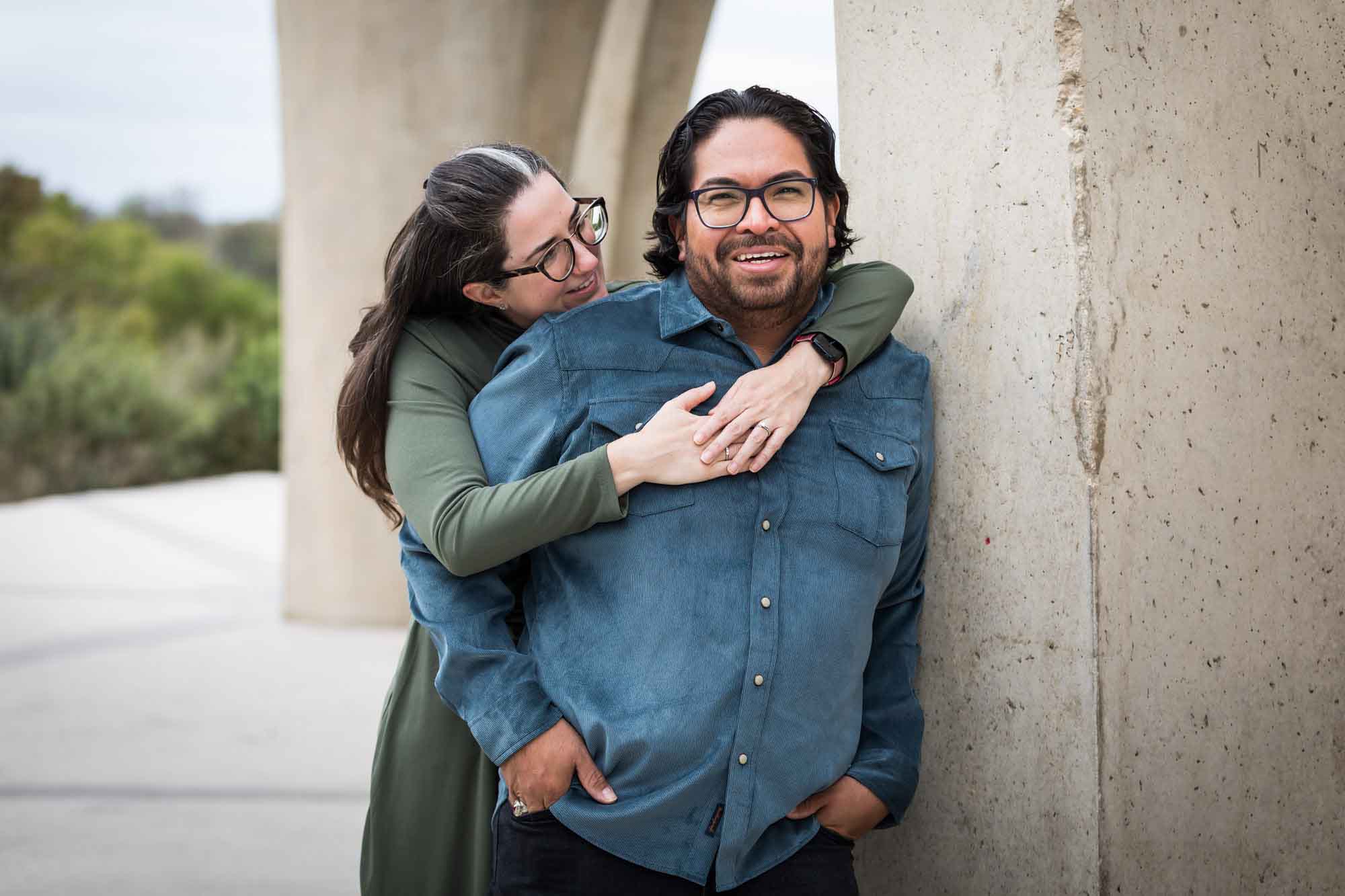 Man wearing denim long-sleeved shirt being hugged by a woman wearing green long-sleeved shirt during a Confluence Park family portrait session