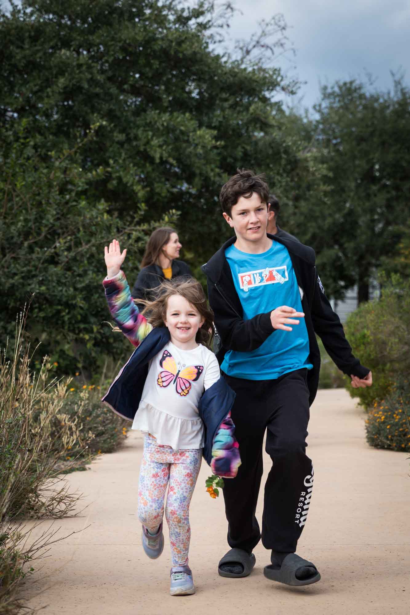 Little girl and older boy running down sidewalk in park during a Confluence Park family portrait session