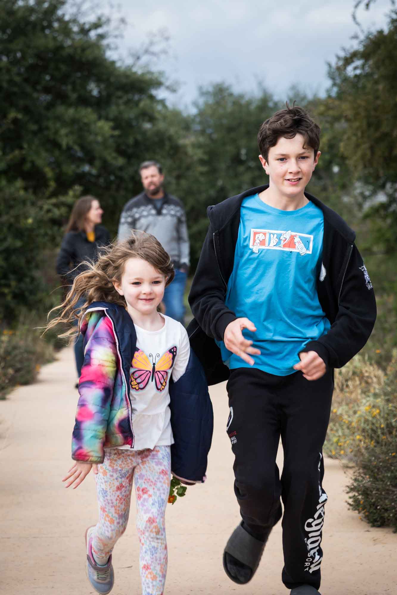 Little girl and older boy running down sidewalk in park during a Confluence Park family portrait session