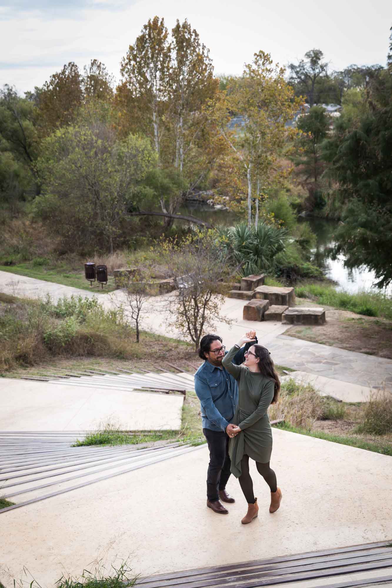 Man wearing denim long-sleeved shirt dancing with woman wearing green dress on stairs during a Confluence Park family portrait session