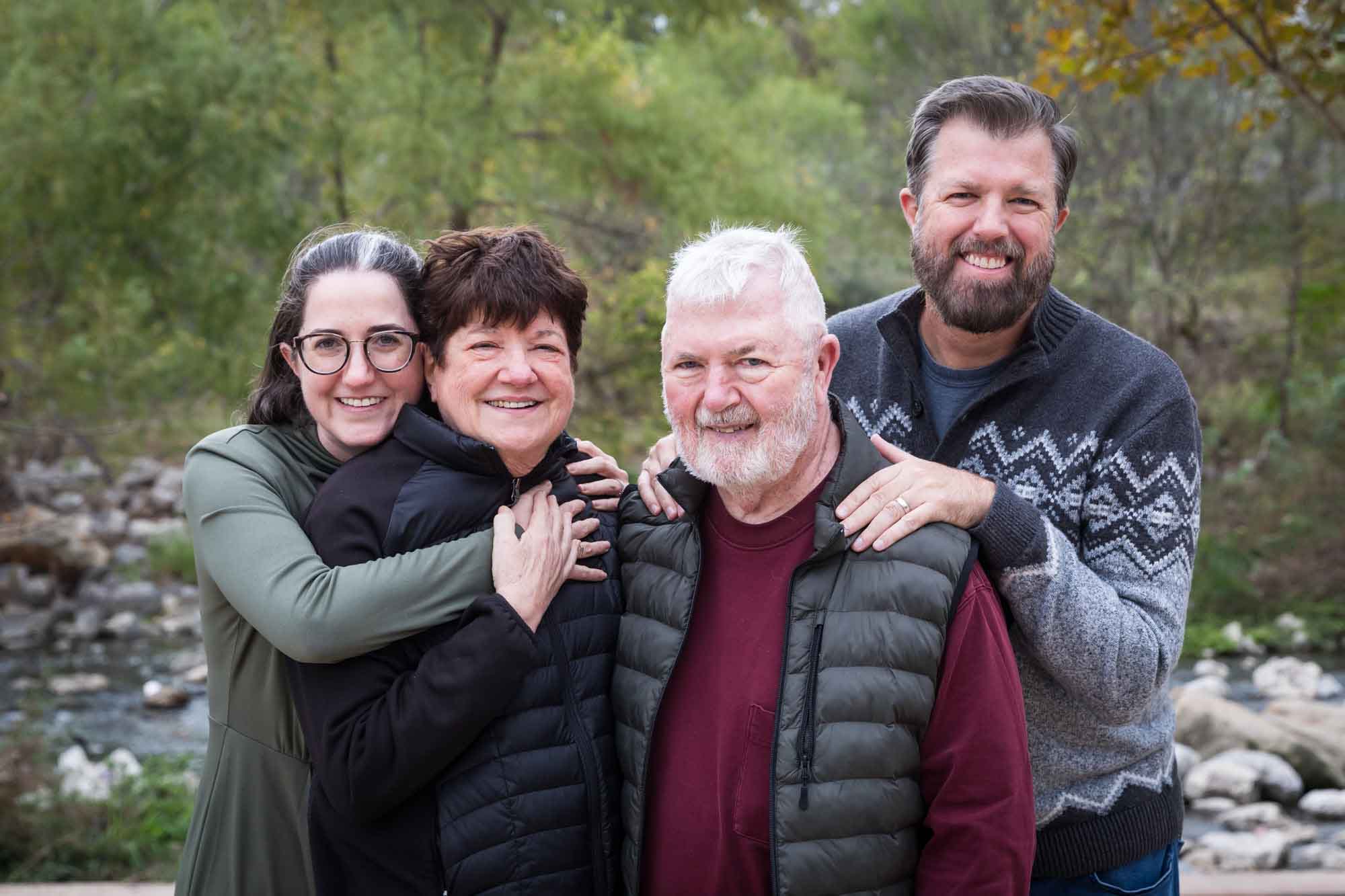 Older parents being hugged by adult children in front of trees during Confluence Park family portrait session