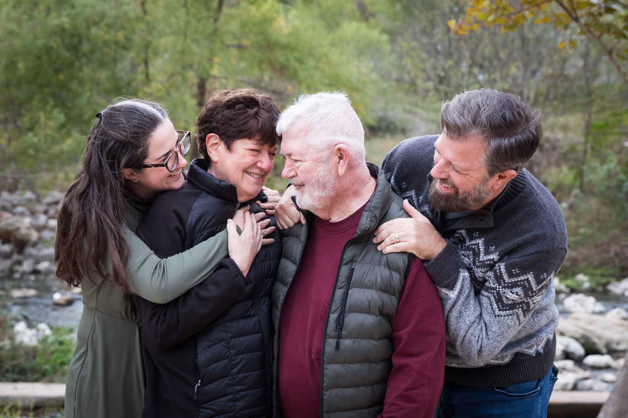 Older parents being hugged by adult children in front of trees during Confluence Park family portrait session