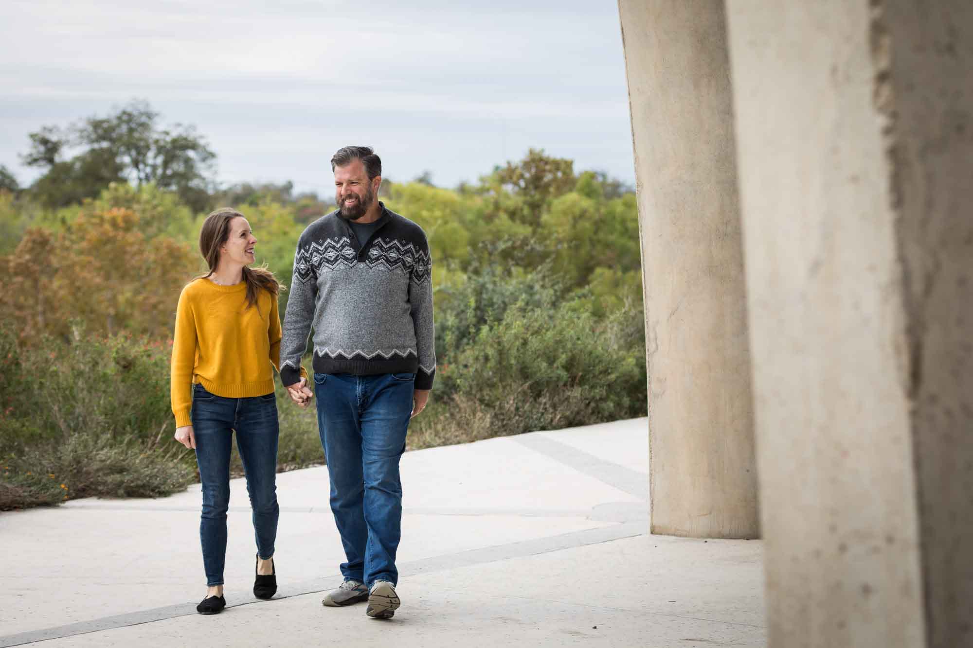 Man wearing grey sweater holding hands with woman wearing yellow sweater and jeans during a Confluence Park family portrait session