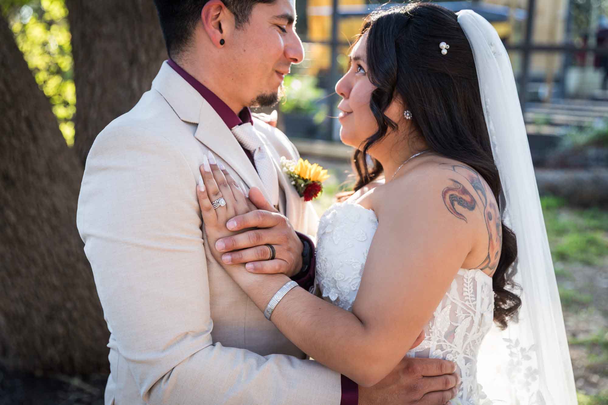 Bride in strapless gown and veil standing close to groom wearing tan suit in front of large oak tree at a San Antonio DIY wedding