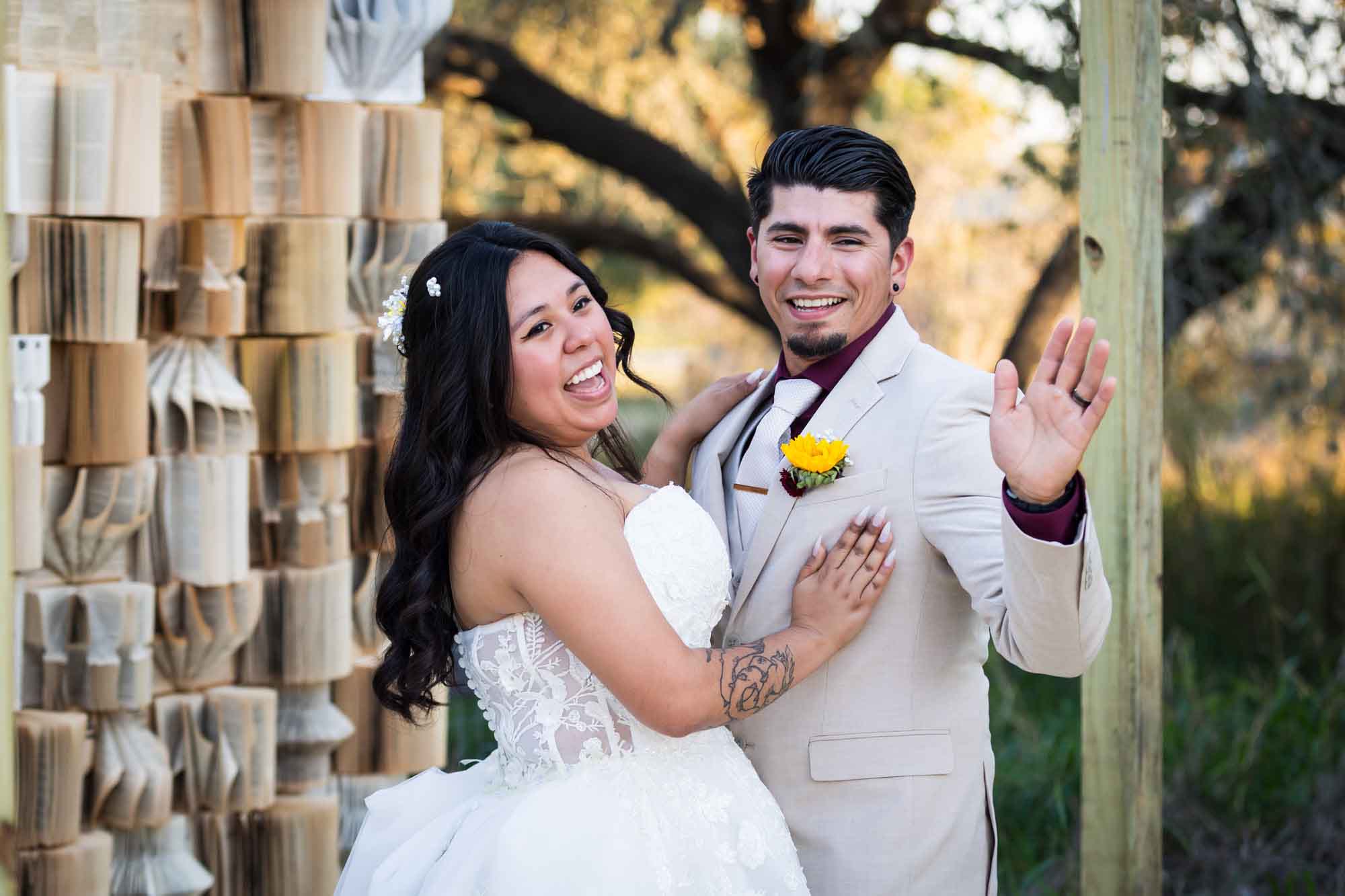 Bride wearing strapless gown laughing with groom wearing tan suit during first dance in front of book background at a San Antonio DIY wedding