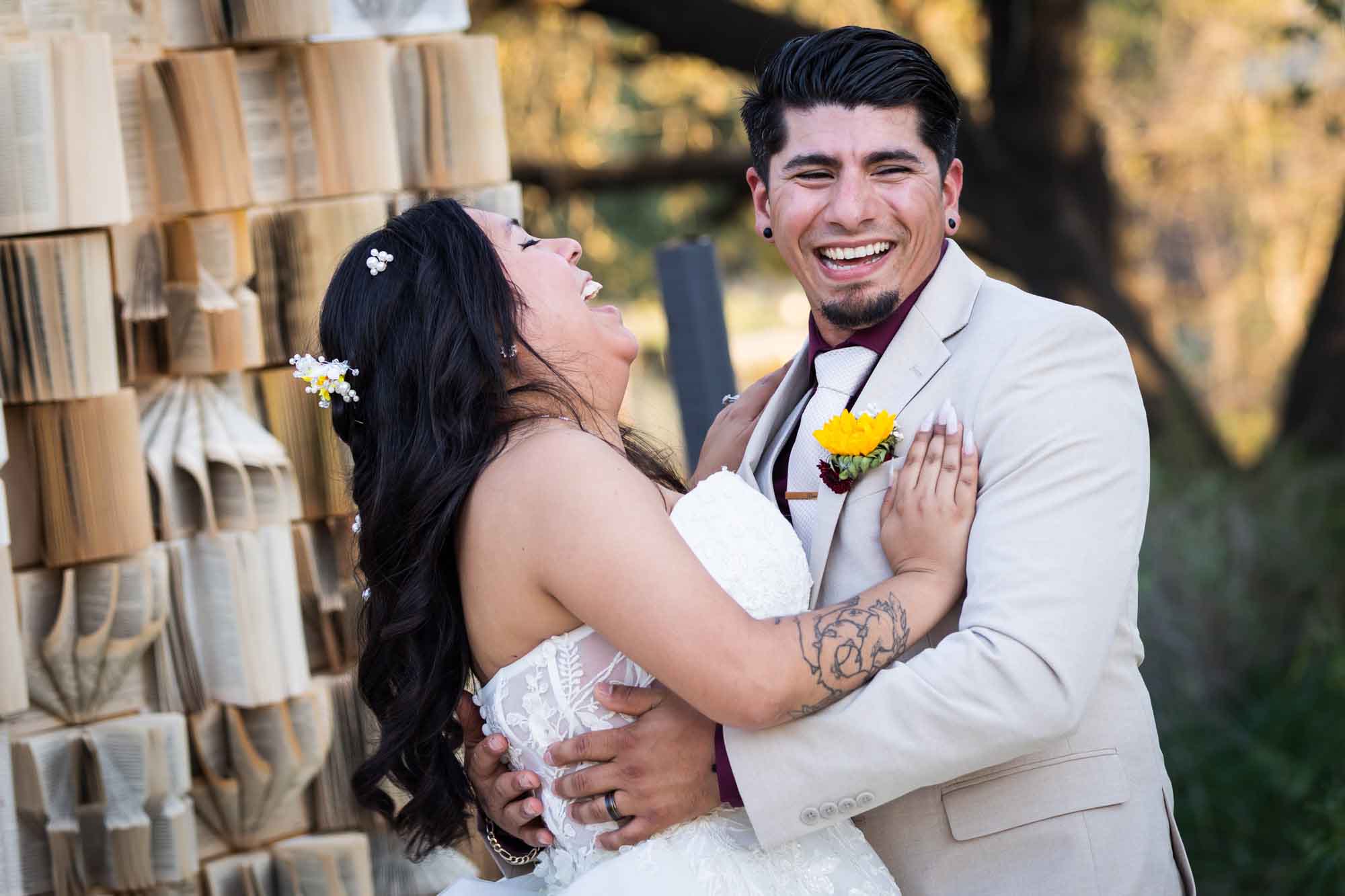 Bride wearing strapless gown laughing with groom wearing tan suit during first dance in front of book background at a San Antonio DIY wedding