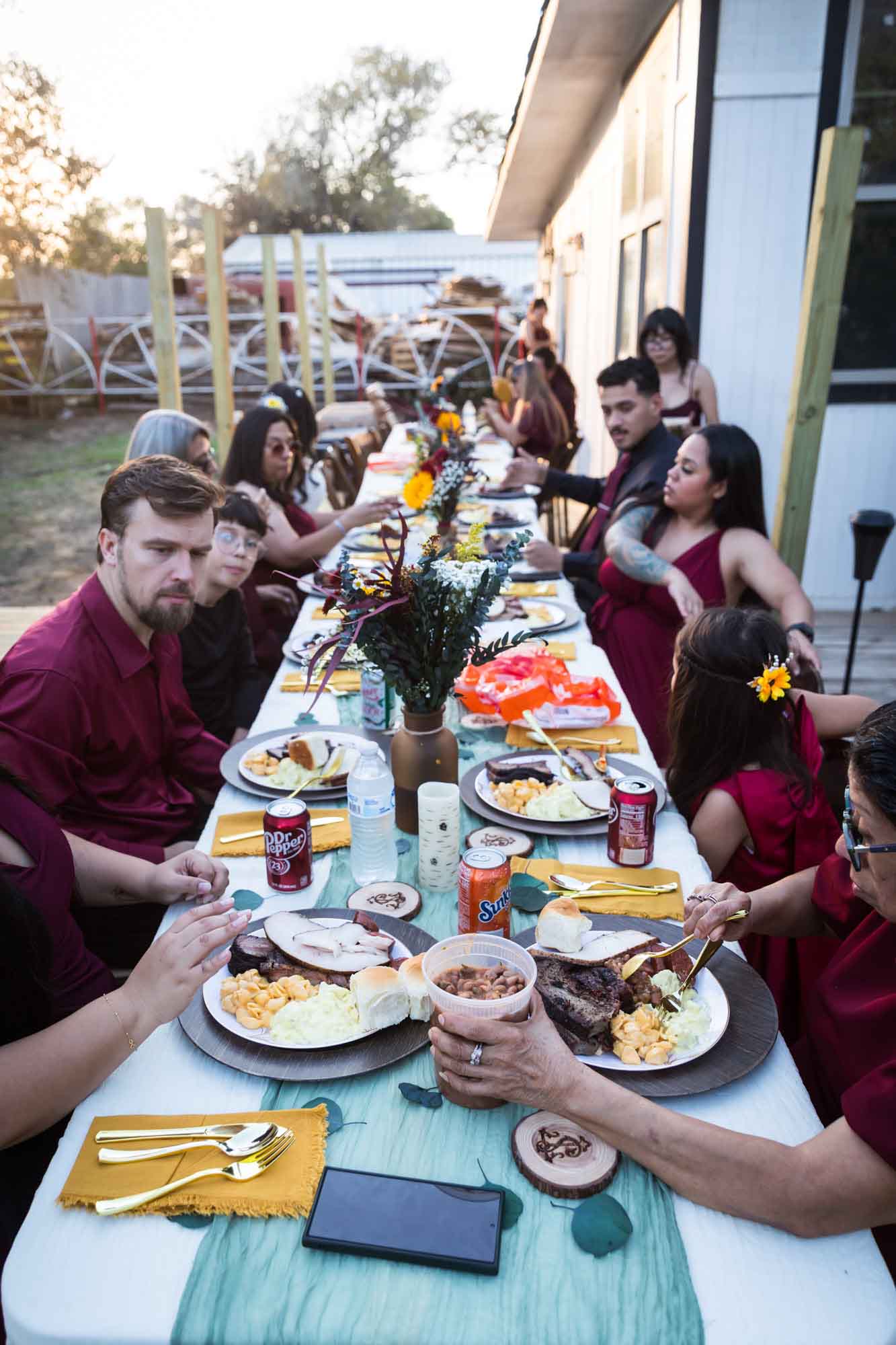 Guests seated at long table eating barbecue during reception outdoors at a San Antonio DIY wedding