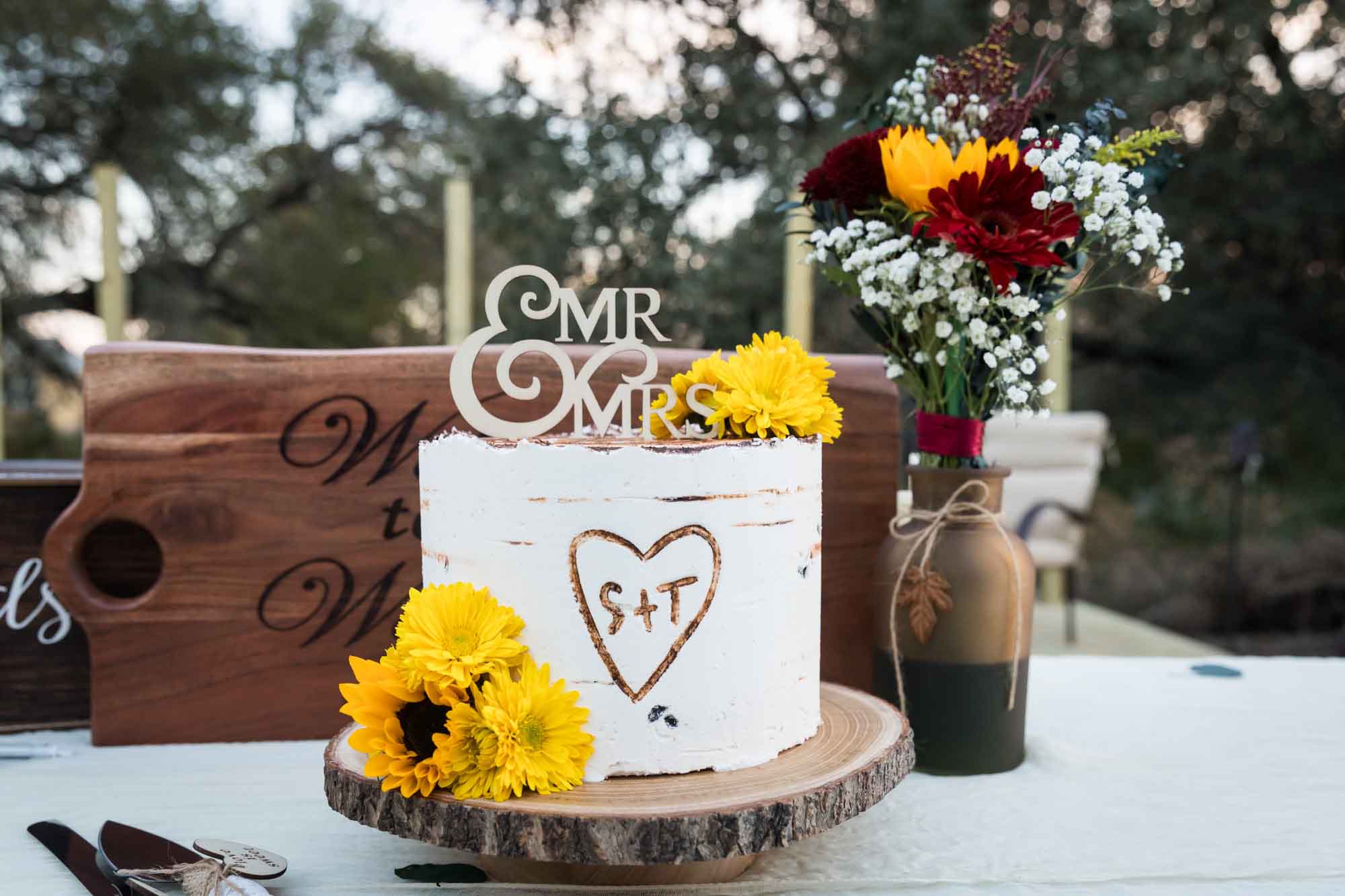 Wedding cake on wooden pedestal with faux wood icing and 'Mr. Mrs.' sign on the top of the cake and yellow flowers at a San Antonio DIY wedding