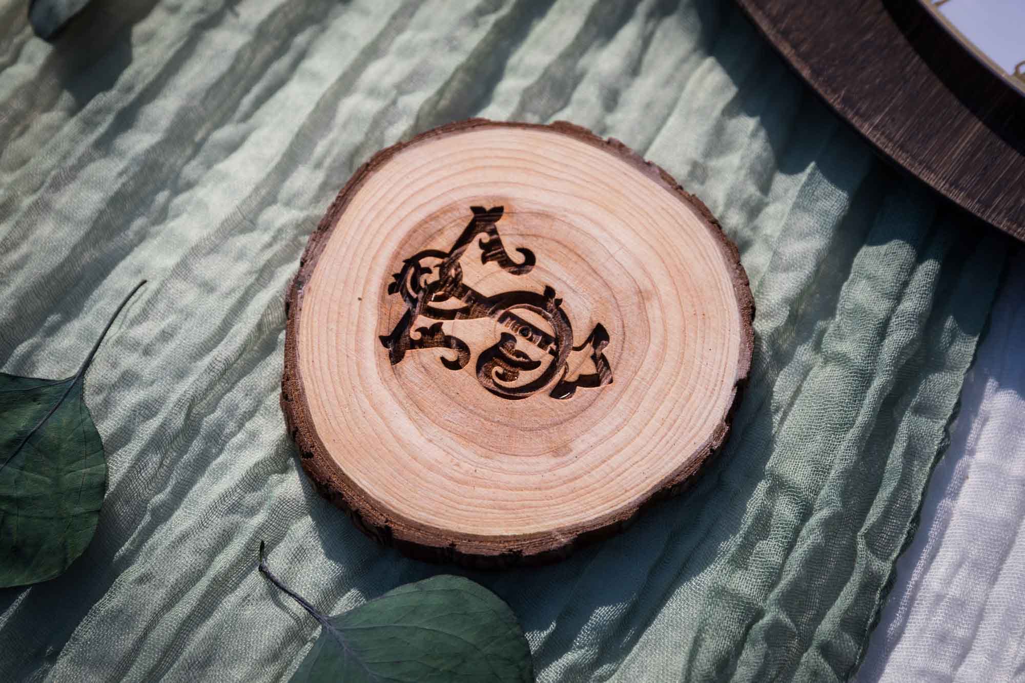 Wooden coaster with intricate monogram on a green cloth table runner at a San Antonio DIY wedding