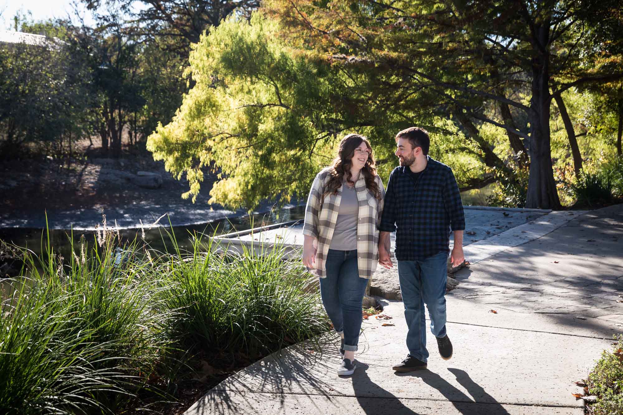 Boerne engagement photos of couple wearing plaid shirts walking and holding hands in River Road Park