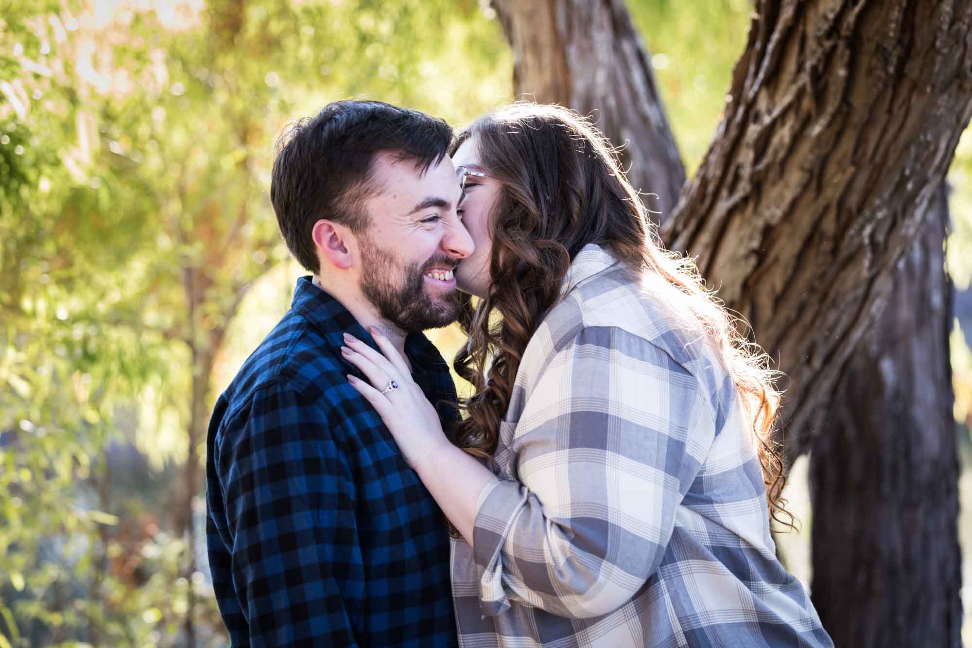 Boerne engagement photos of couple wearing plaid shirts kissing in front of trees in River Road Park