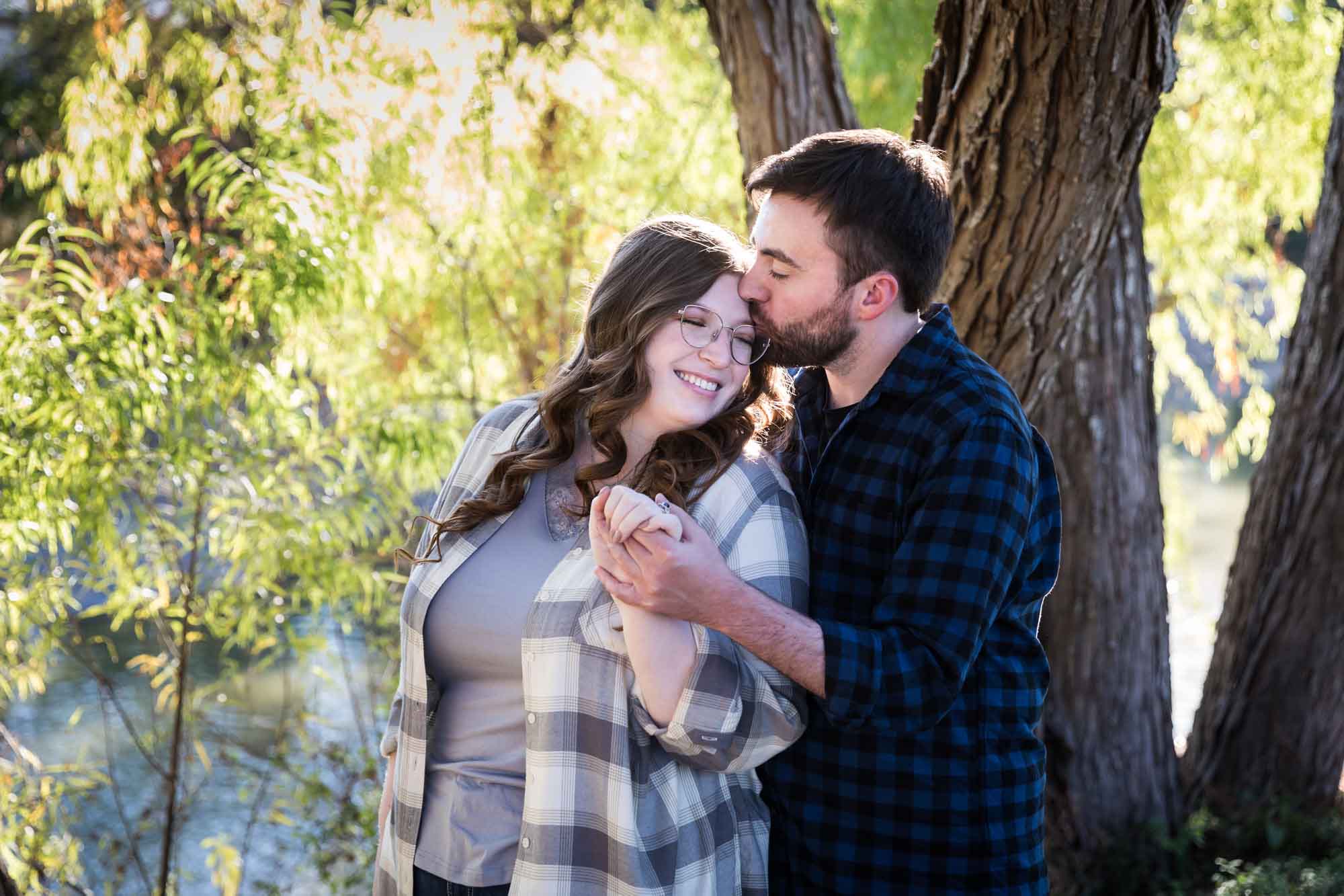 Boerne engagement photos of couple wearing plaid shirts hugging in front of trees in River Road Park