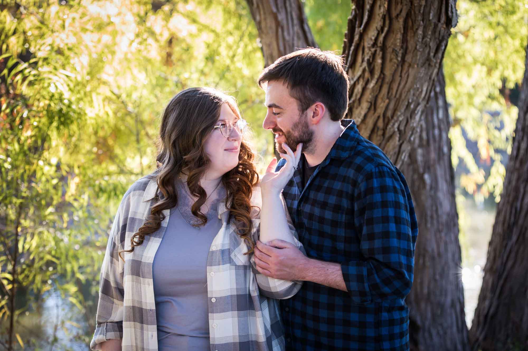 Boerne engagement photos of couple wearing plaid shirts hugging in front of trees in River Road Park
