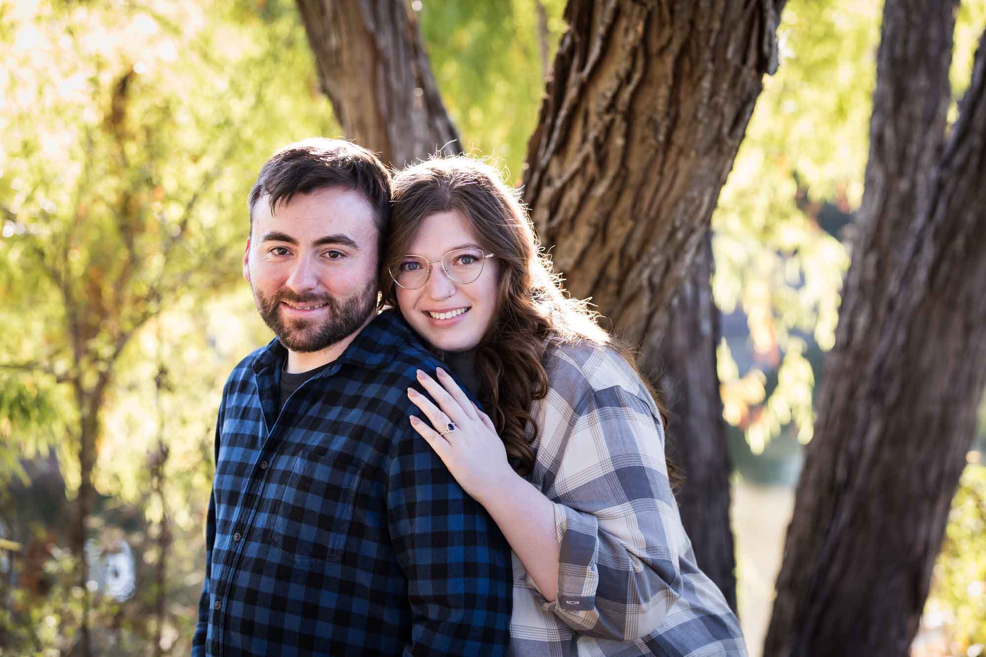 Boerne engagement photos of couple wearing plaid shirts hugging in front of trees in River Road Park