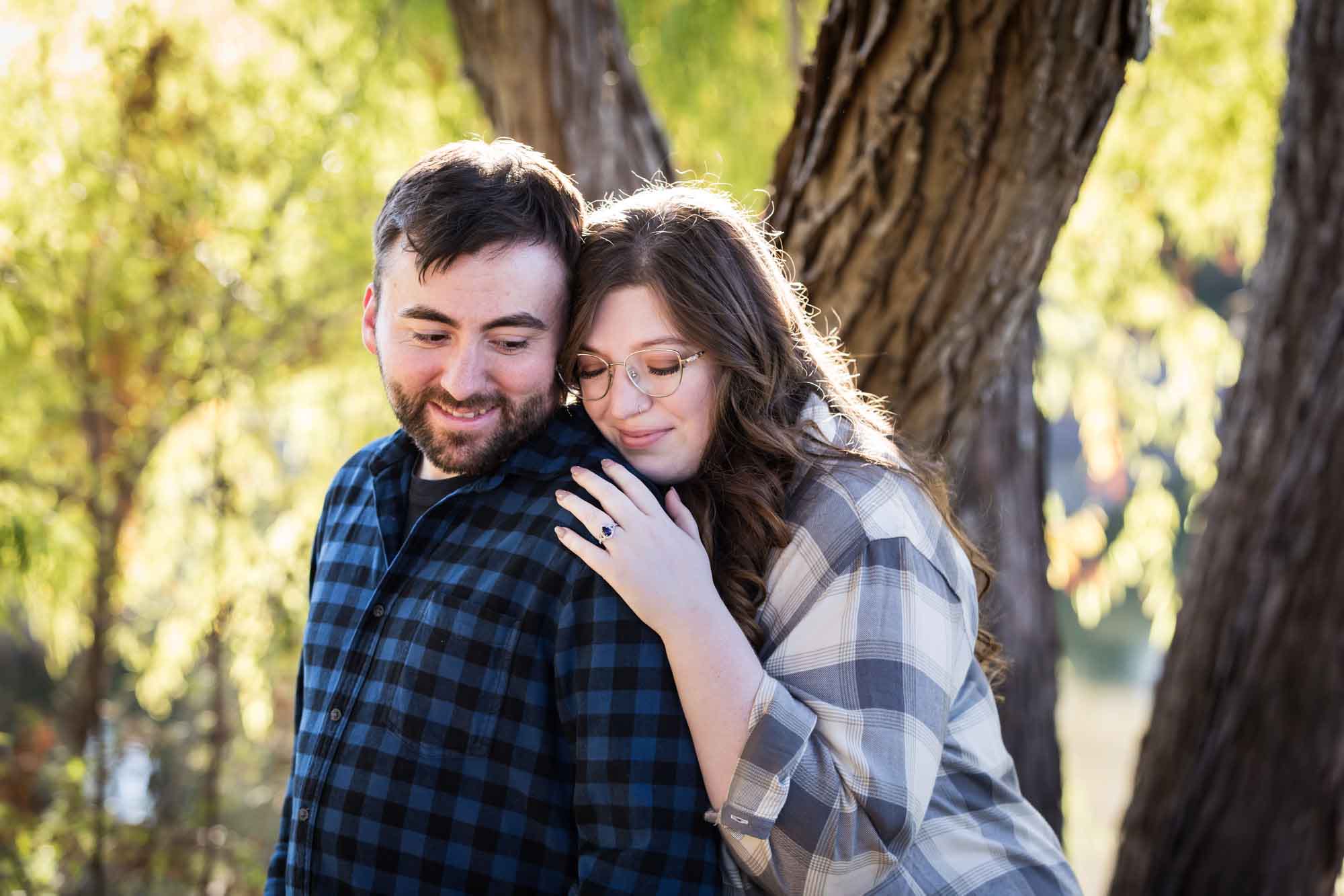 Boerne engagement photos of couple wearing plaid shirts hugging in front of trees in River Road Park
