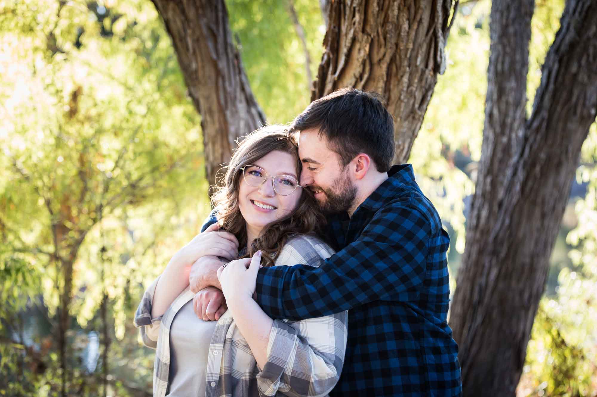 Boerne engagement photos of couple wearing plaid shirts hugging in front of trees in River Road Park