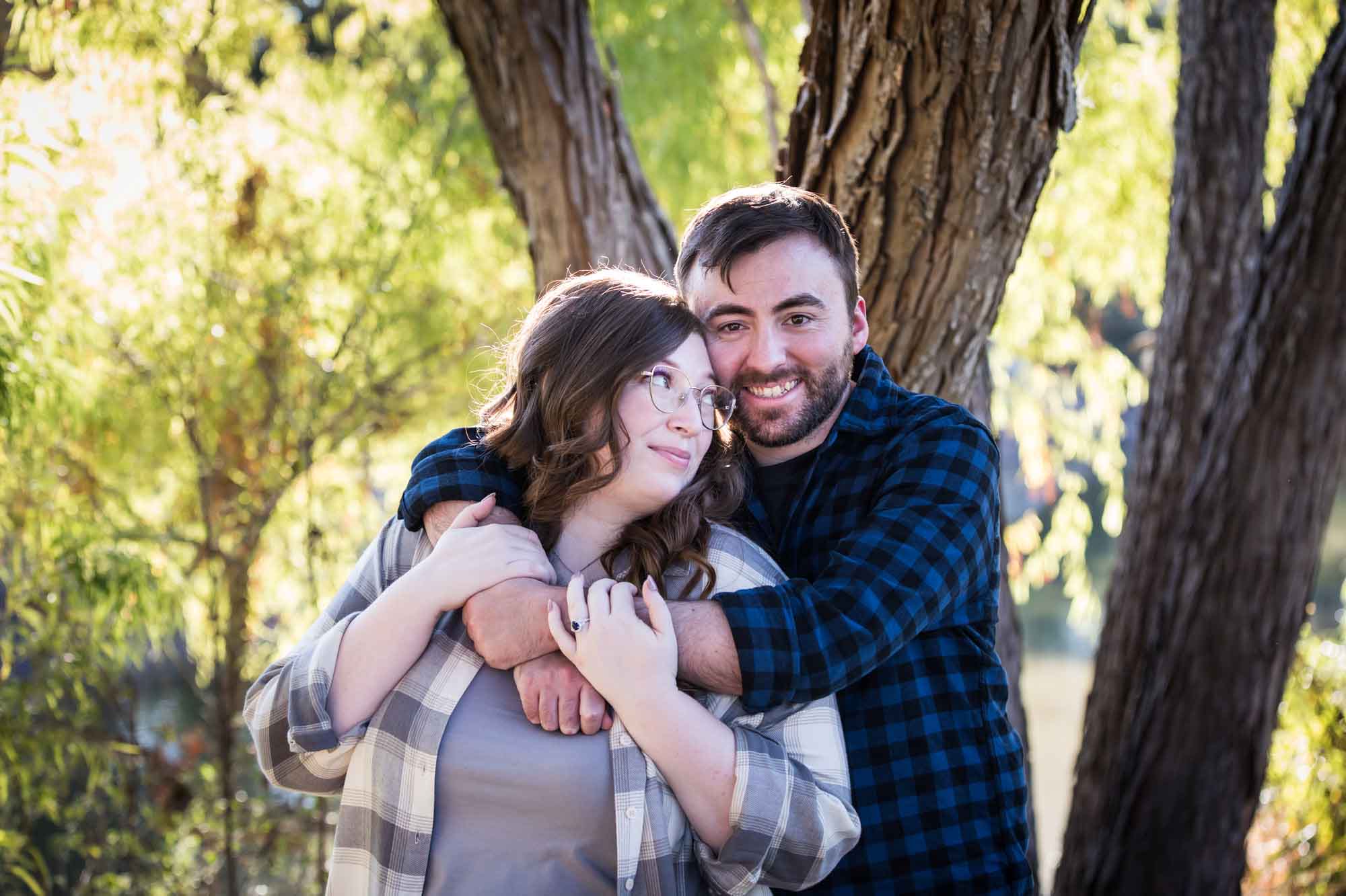 Boerne engagement photos of couple wearing plaid shirts hugging in front of trees in River Road Park
