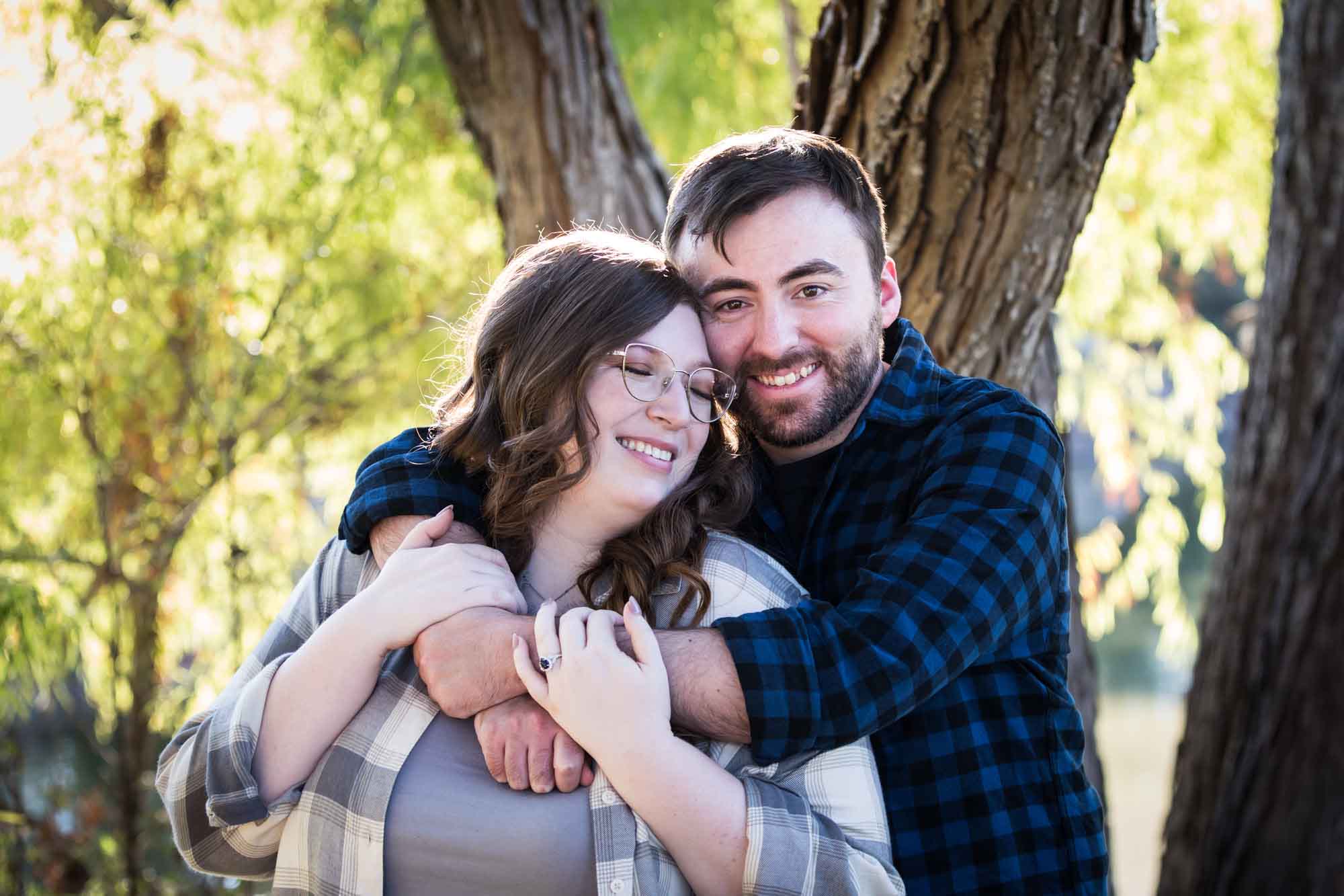 Boerne engagement photos of couple wearing plaid shirts hugging in front of trees in River Road Park