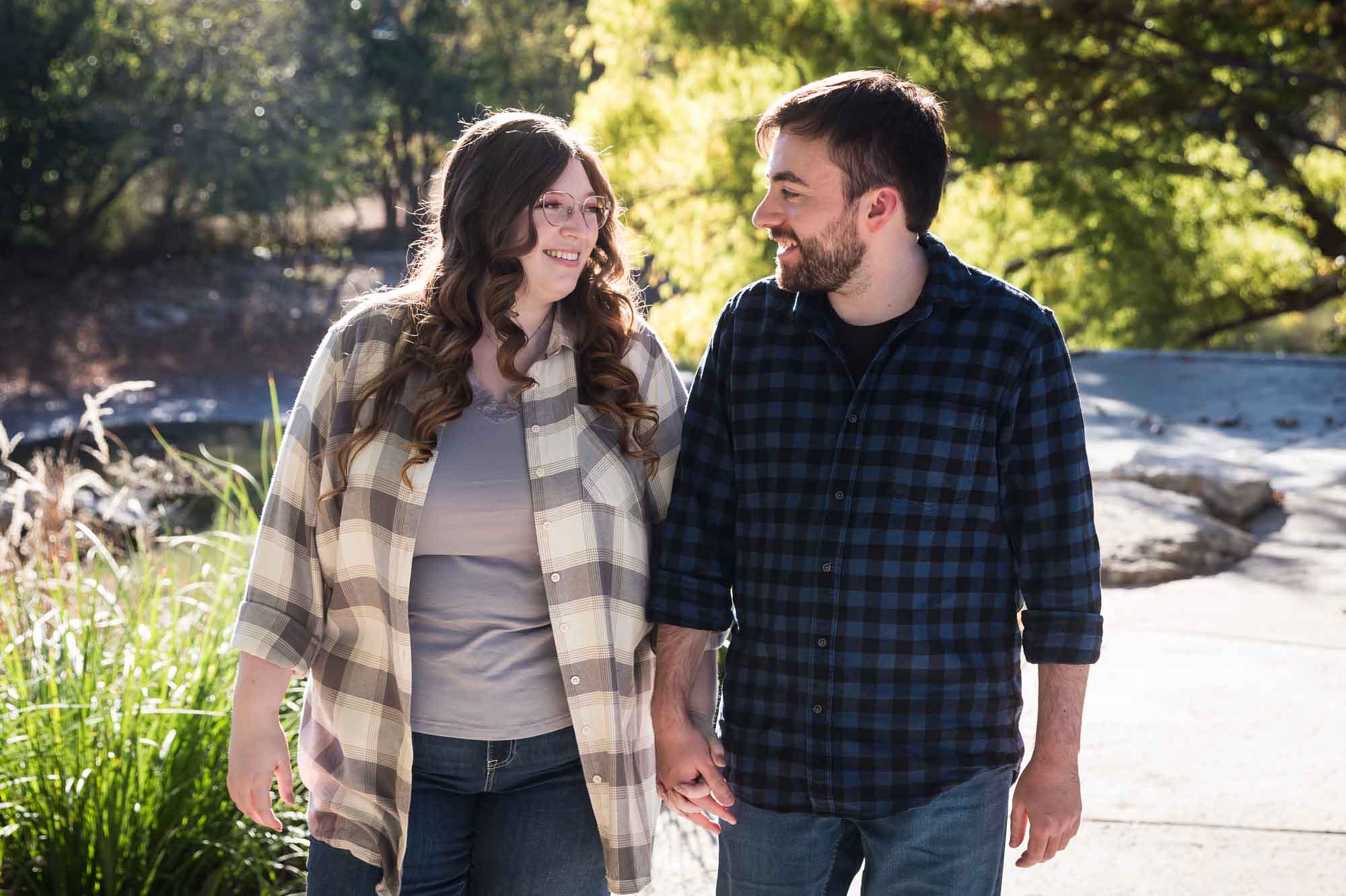 Boerne engagement photos of couple wearing plaid shirts walking and holding hands in River Road Park