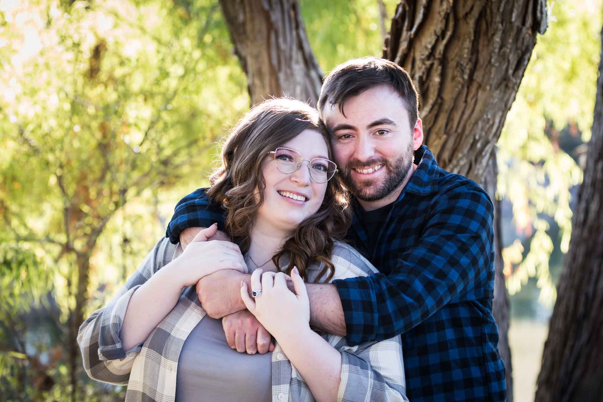Boerne engagement photos of couple wearing plaid shirts hugging in front of trees in River Road Park