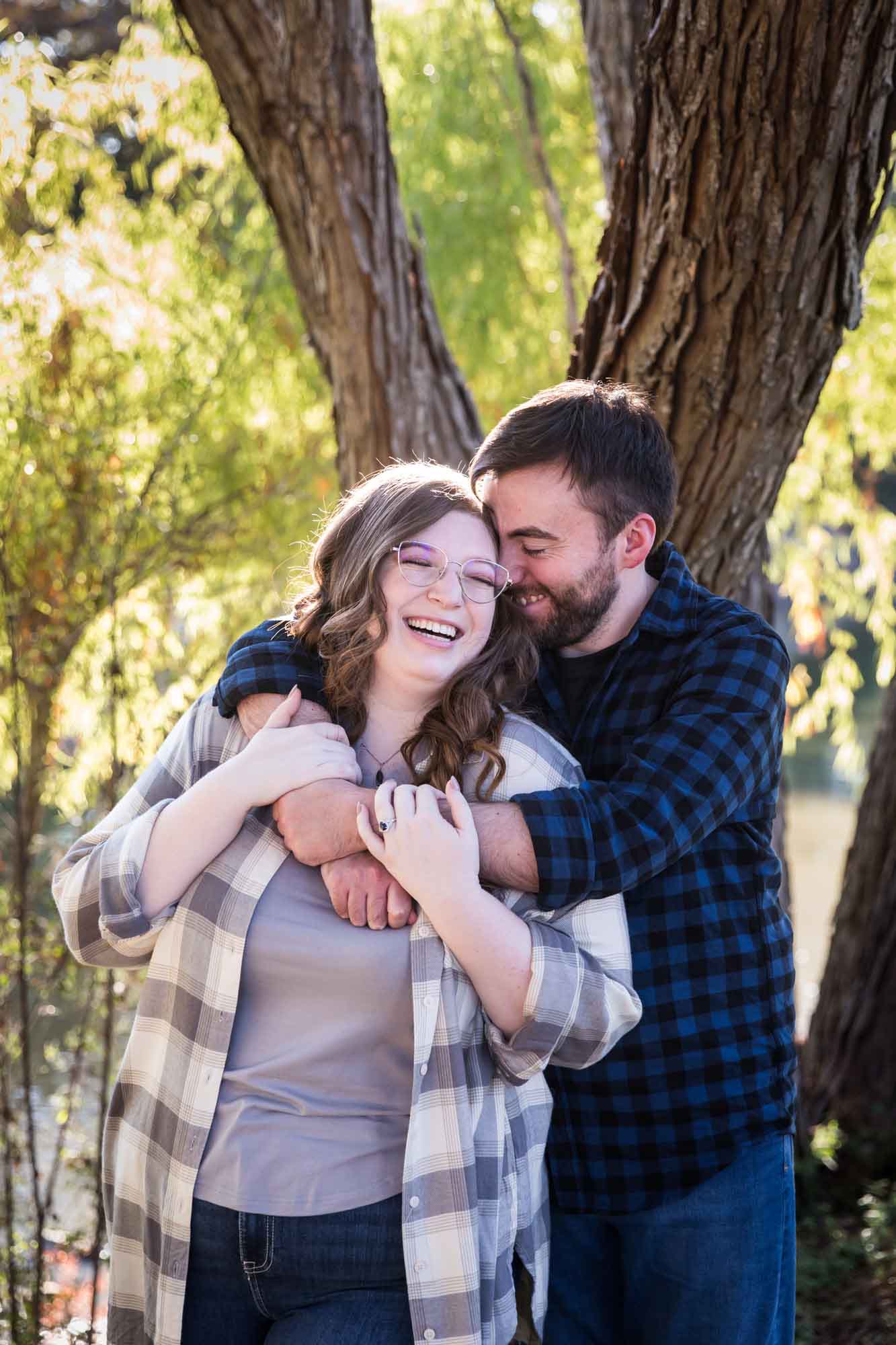 Boerne engagement photos of couple wearing plaid shirts hugging in front of trees in River Road Park
