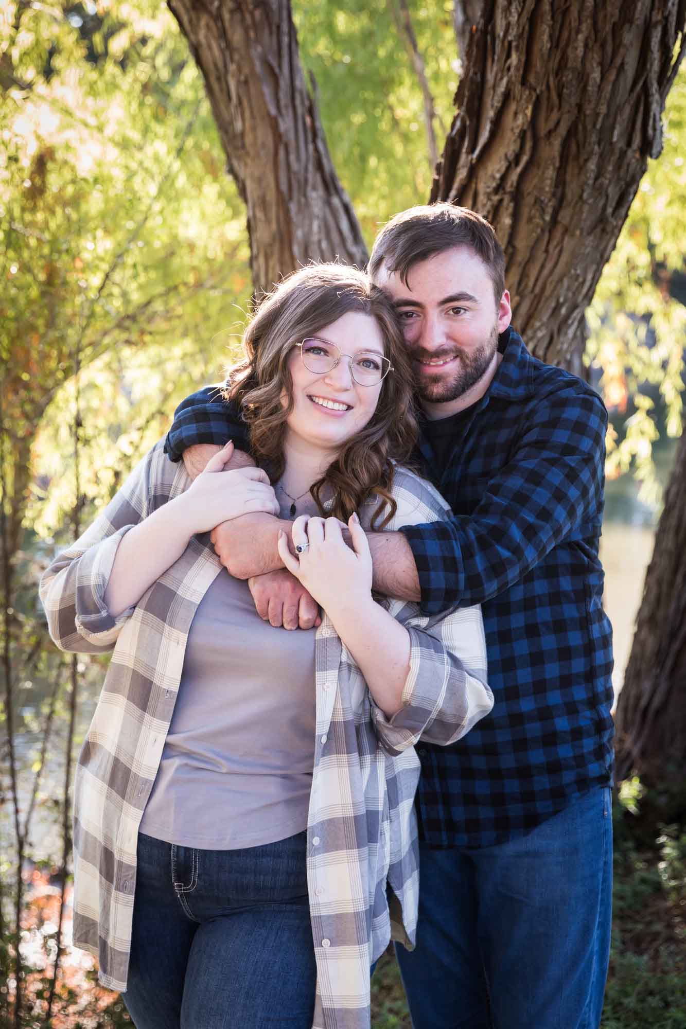 Boerne engagement photos of couple wearing plaid shirts hugging in front of trees in River Road Park