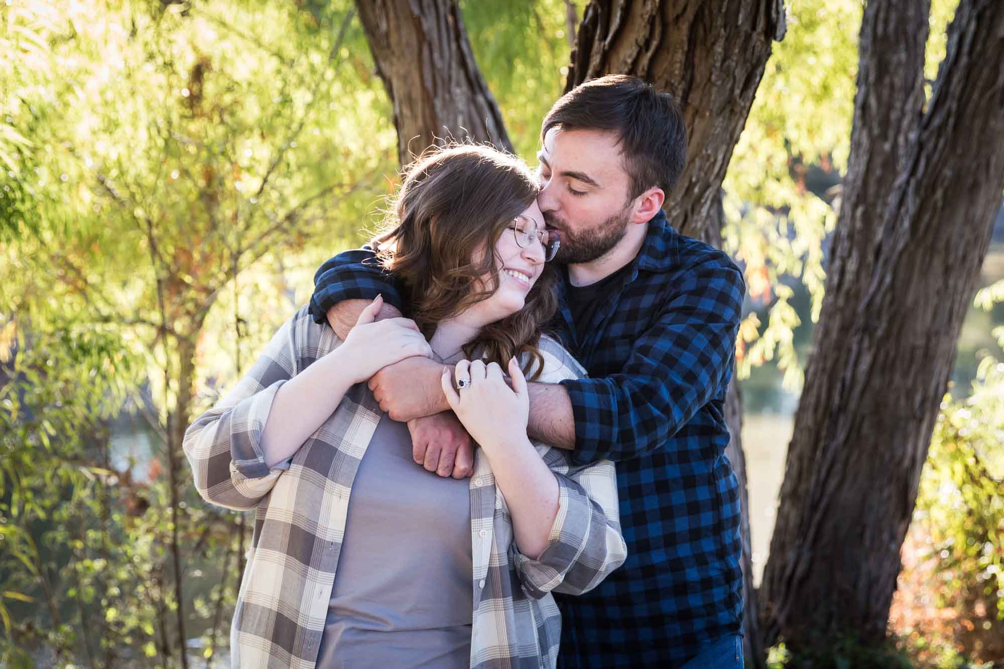 Boerne engagement photos of couple wearing plaid shirts hugging in front of trees in River Road Park