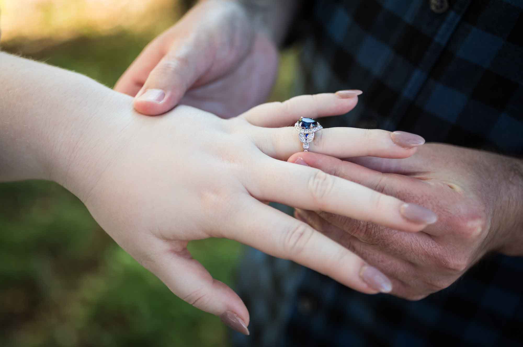 Close up of man putting engagement ring with blue sapphire on woman's hand