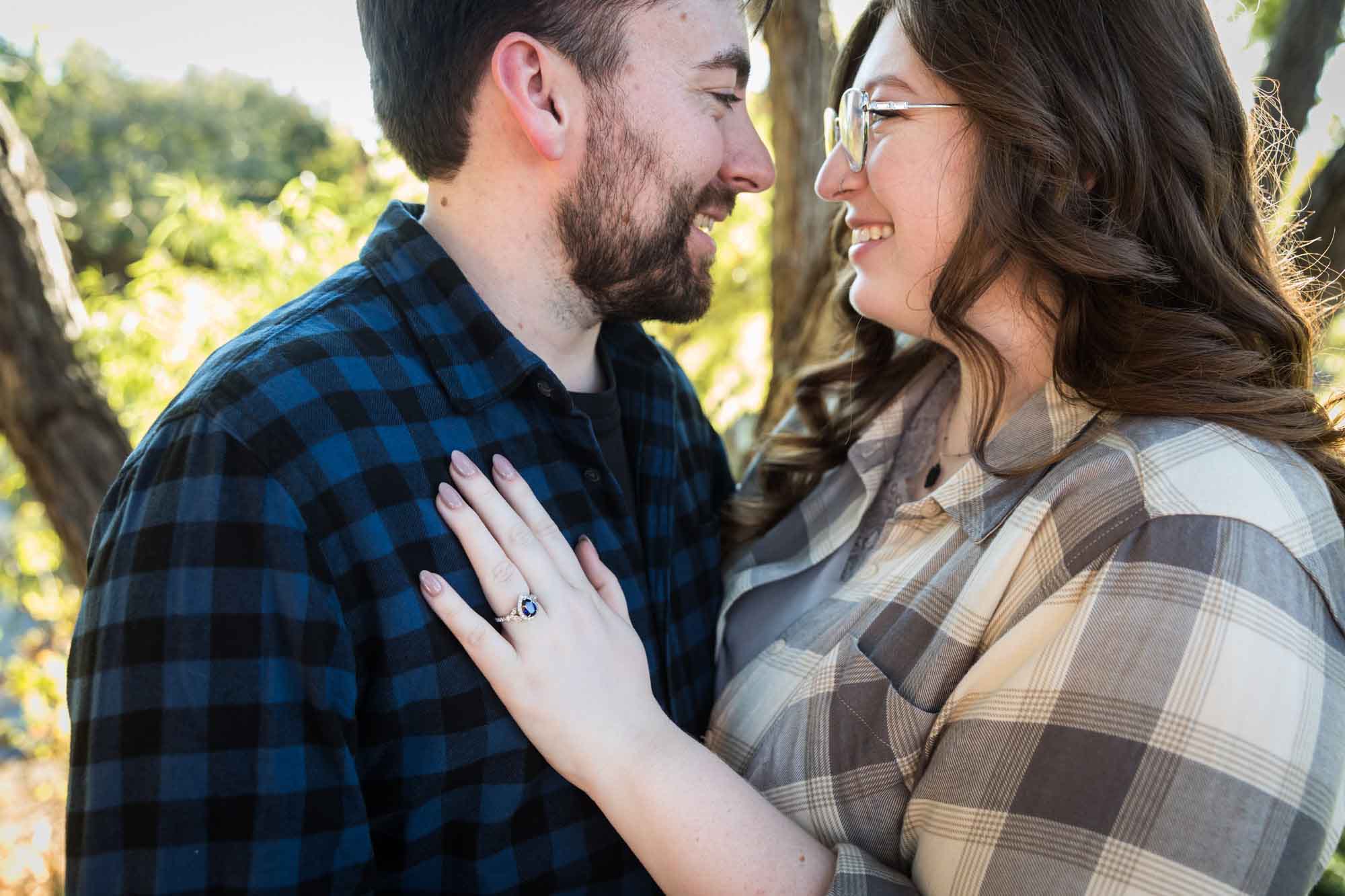 Boerne engagement photos of couple wearing plaid shirts hugging in front of trees in River Road Park