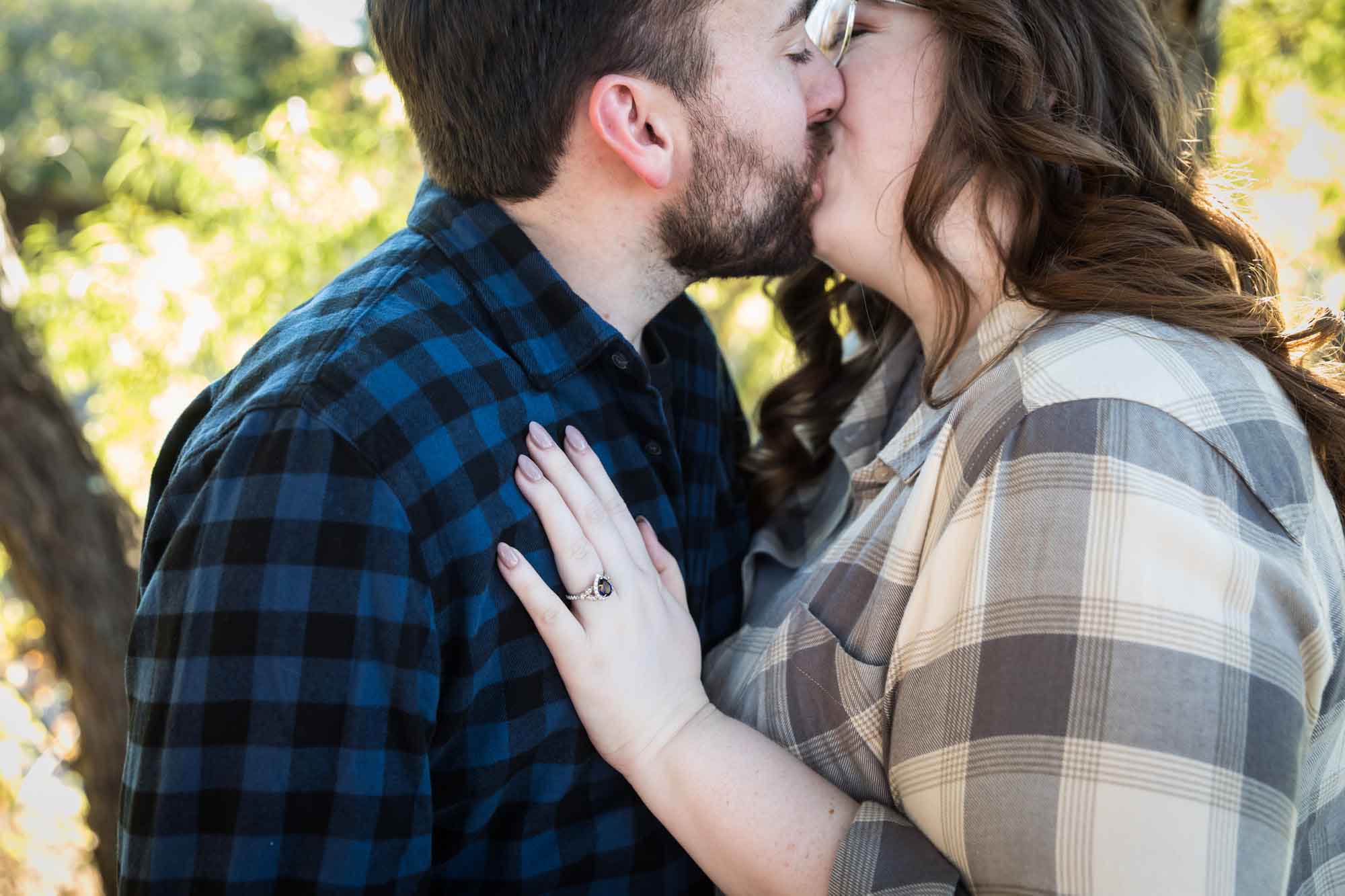 Boerne engagement photos of couple wearing plaid shirts kissing in front of trees in River Road Park