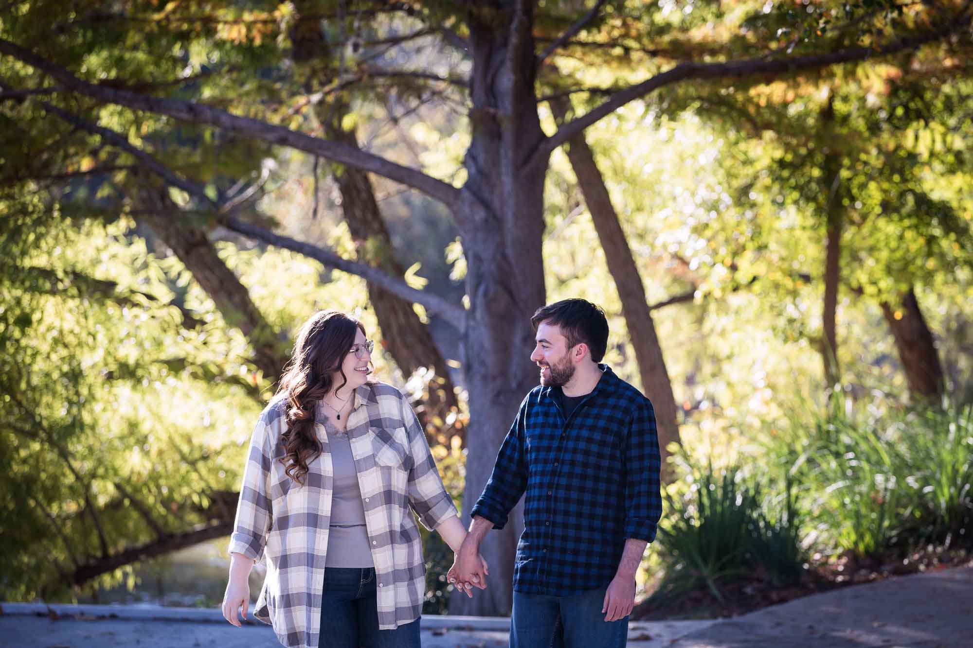 Boerne engagement photos of couple wearing plaid shirts walking and holding hands in River Road Park