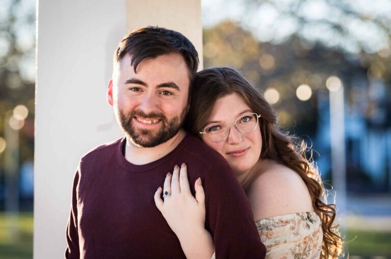 Boerne engagement photos of woman hugging man from behind in front of white column in Main Plaza